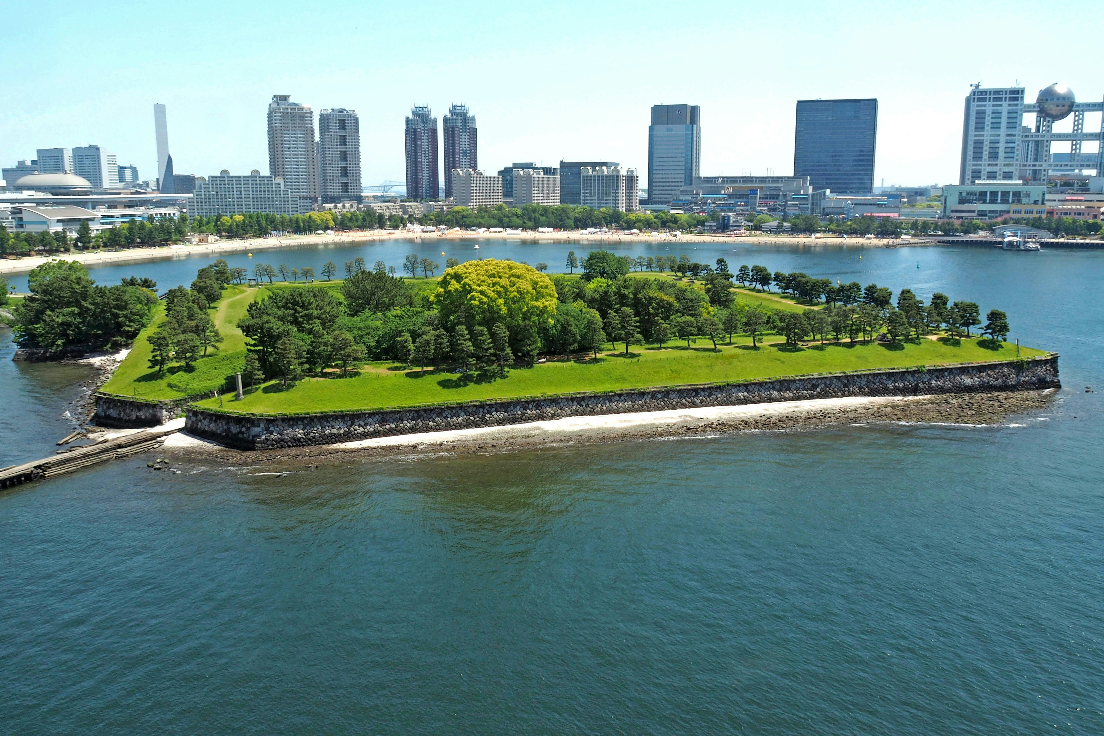 A green island surrounded by blue water with a city skyline in the background