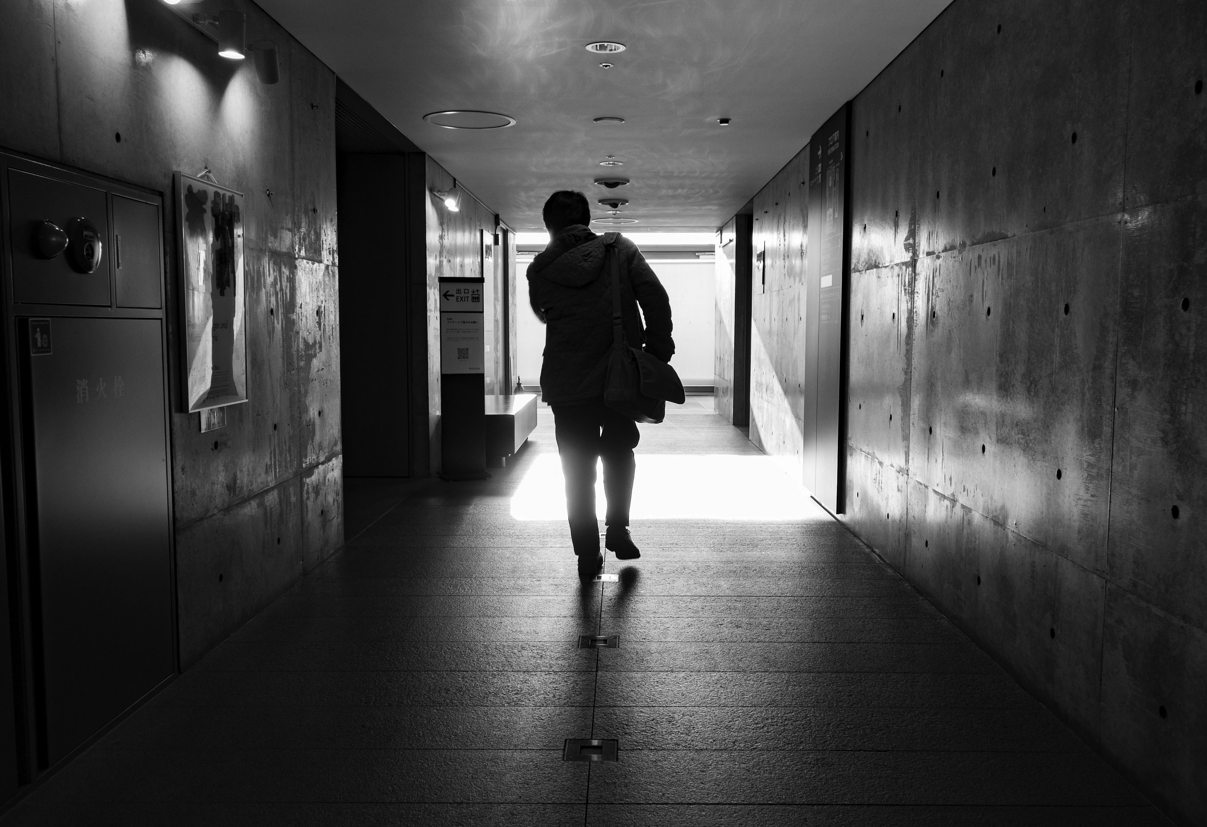 Silhouette of a person walking down a corridor with concrete walls and bright light