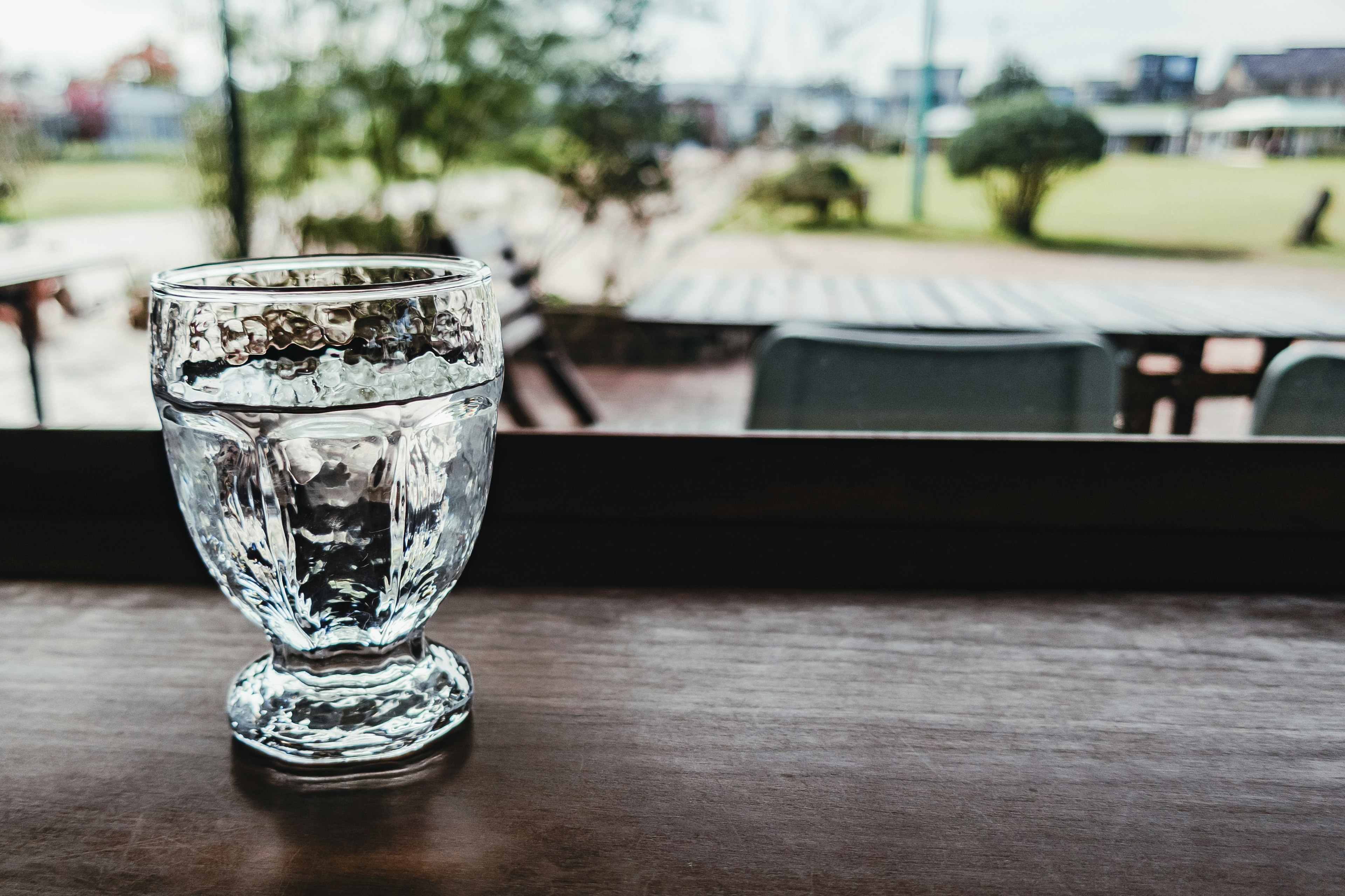 Gelas air bening dengan pemandangan taman hijau di kafe