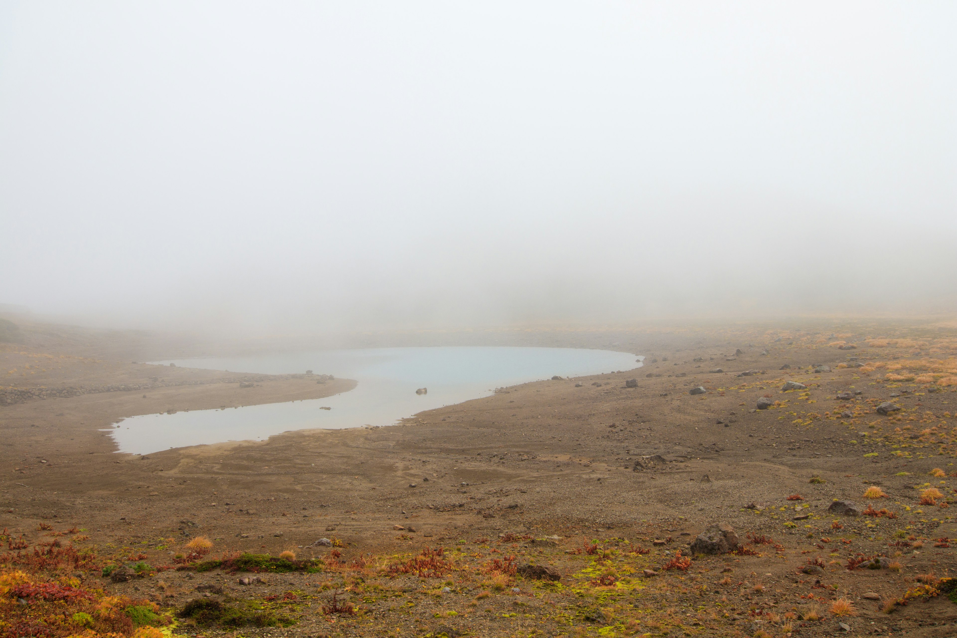 Fog-covered landscape with a small pond on a barren terrain