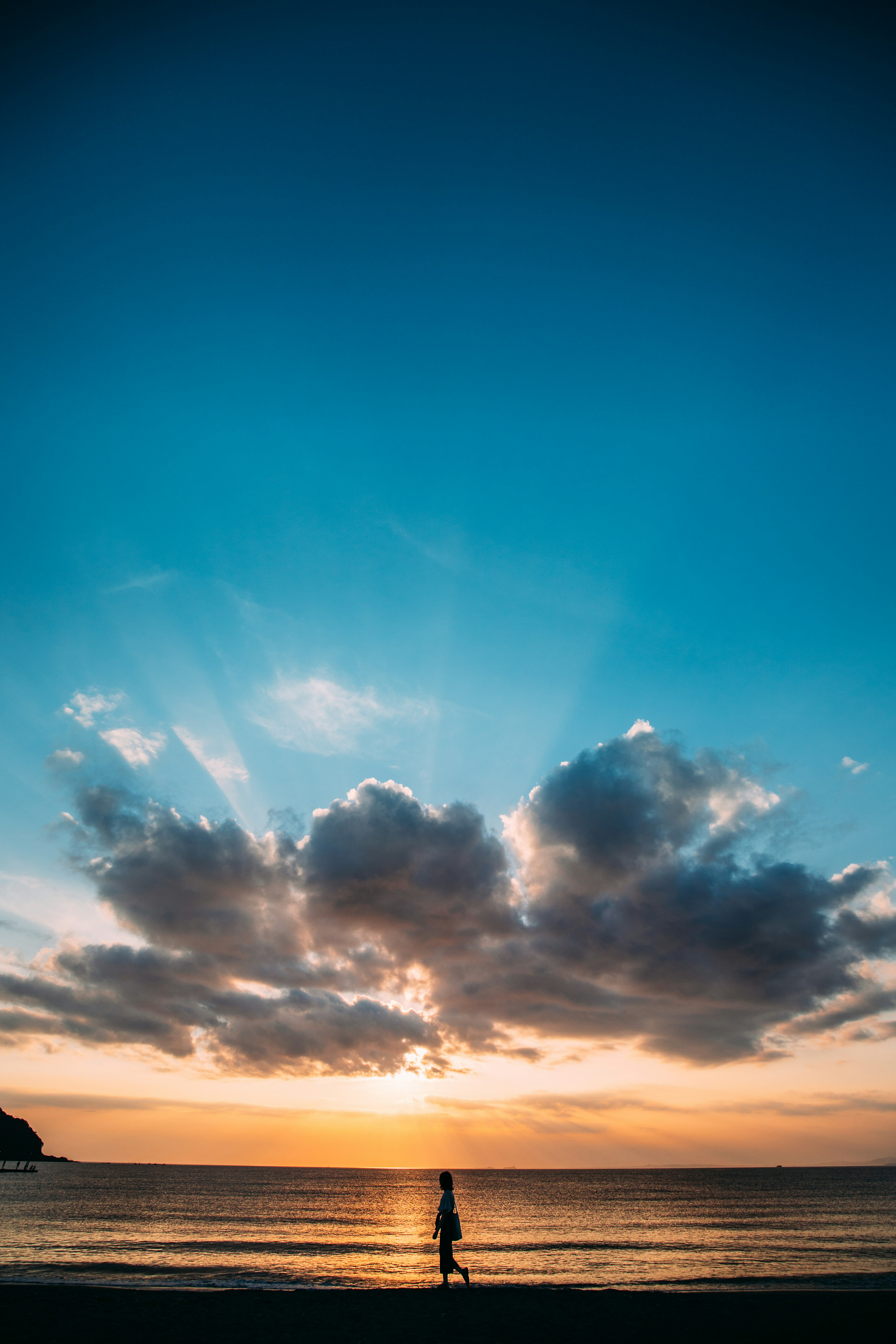 海辺で夕日を背にして歩く人のシルエット青い空と雲の景色