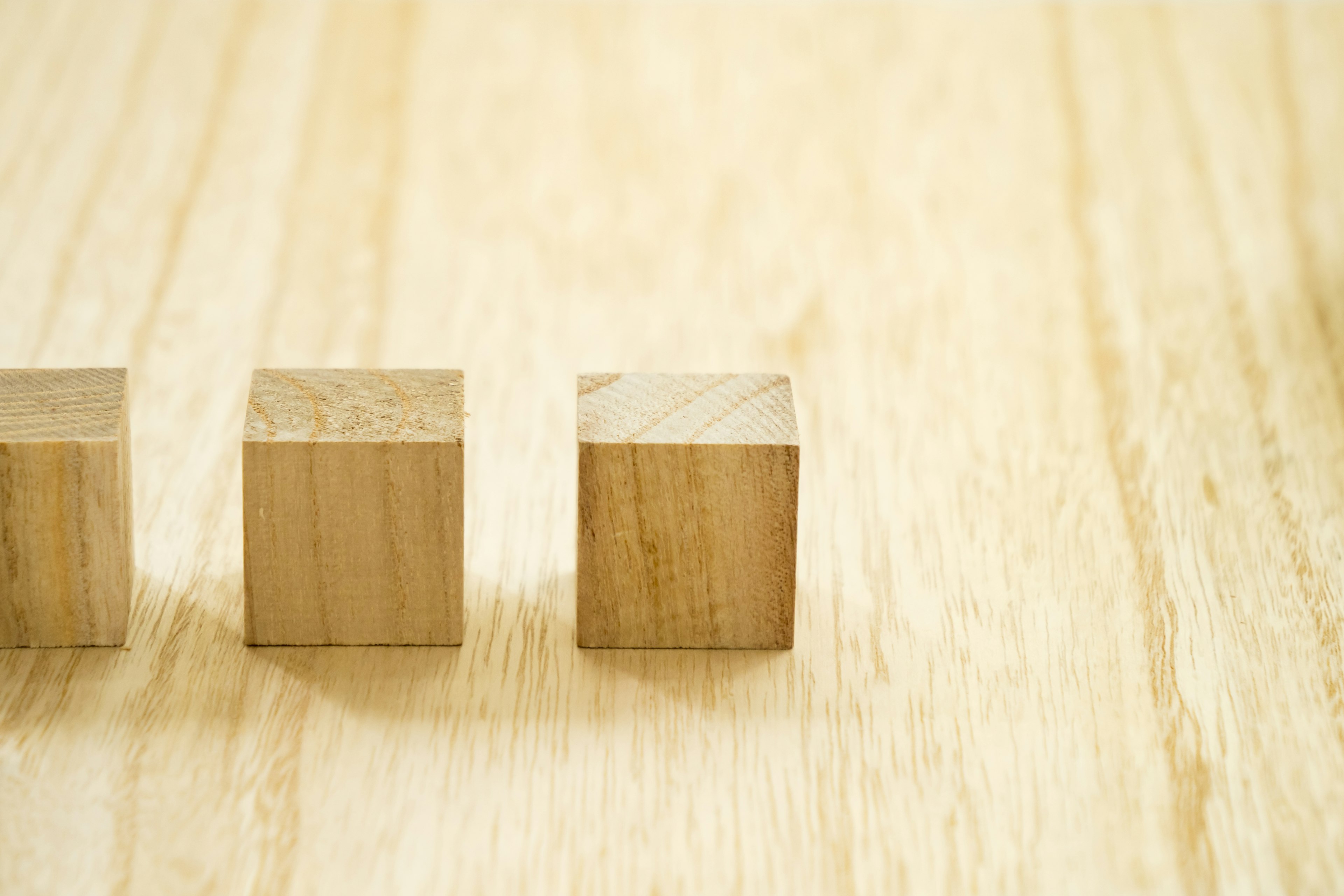 Trois cubes en bois alignés sur une surface en bois clair