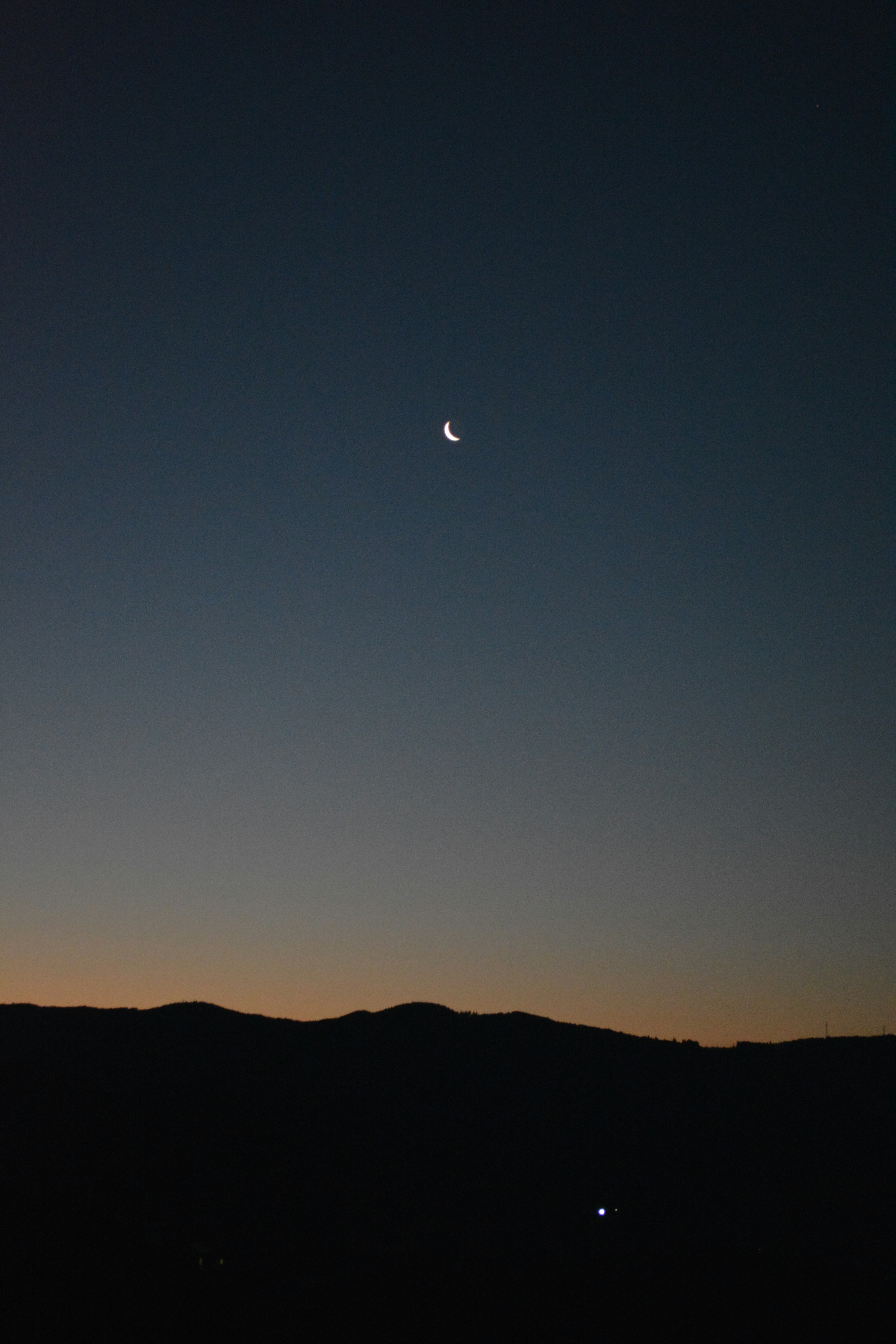 Luna crescente nel cielo notturno con silhouette di montagne