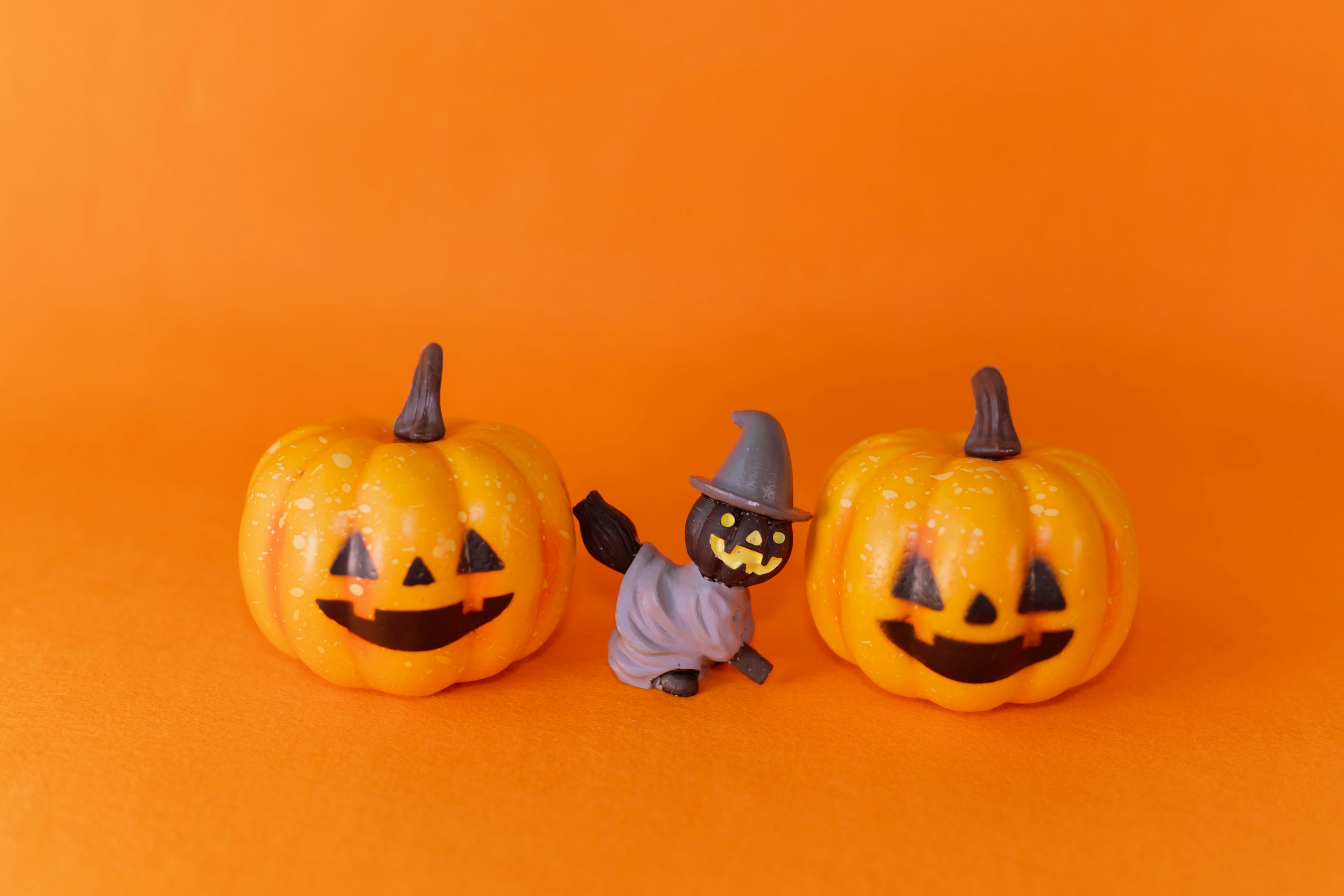 Two jack-o'-lanterns with a small witch figure in front on an orange background