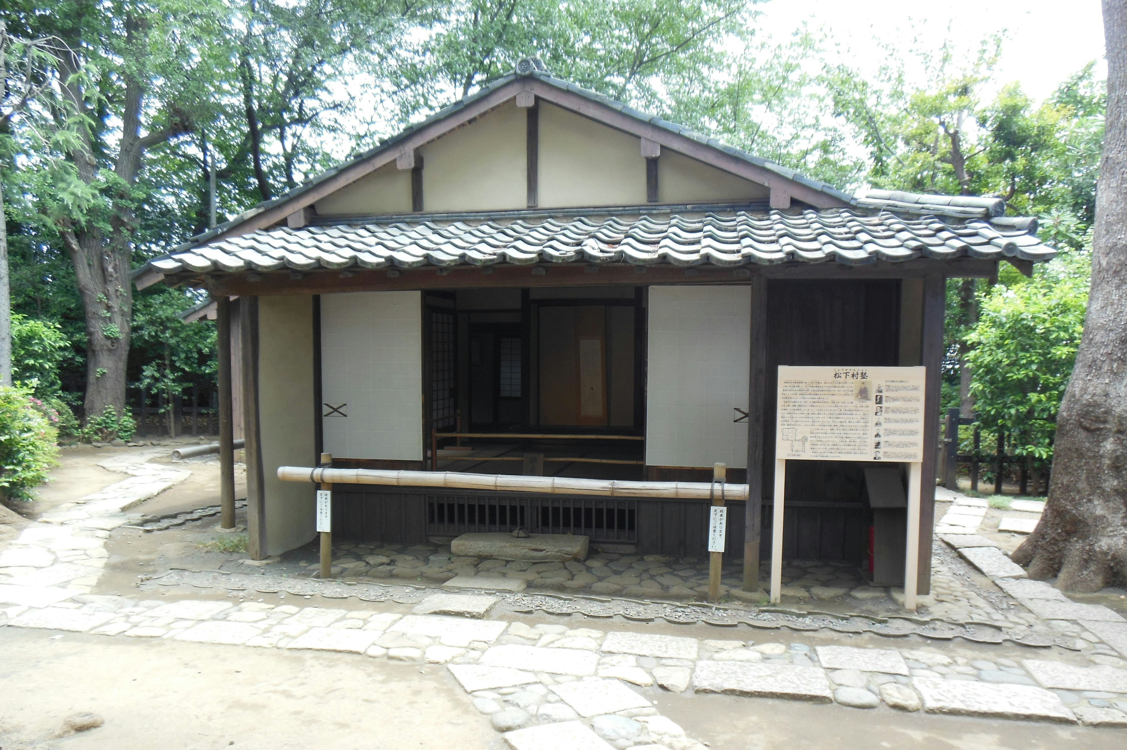 Außenansicht eines traditionellen japanischen Hauses mit einem mit Ziegeln gedeckten Dach, umgeben von Grün