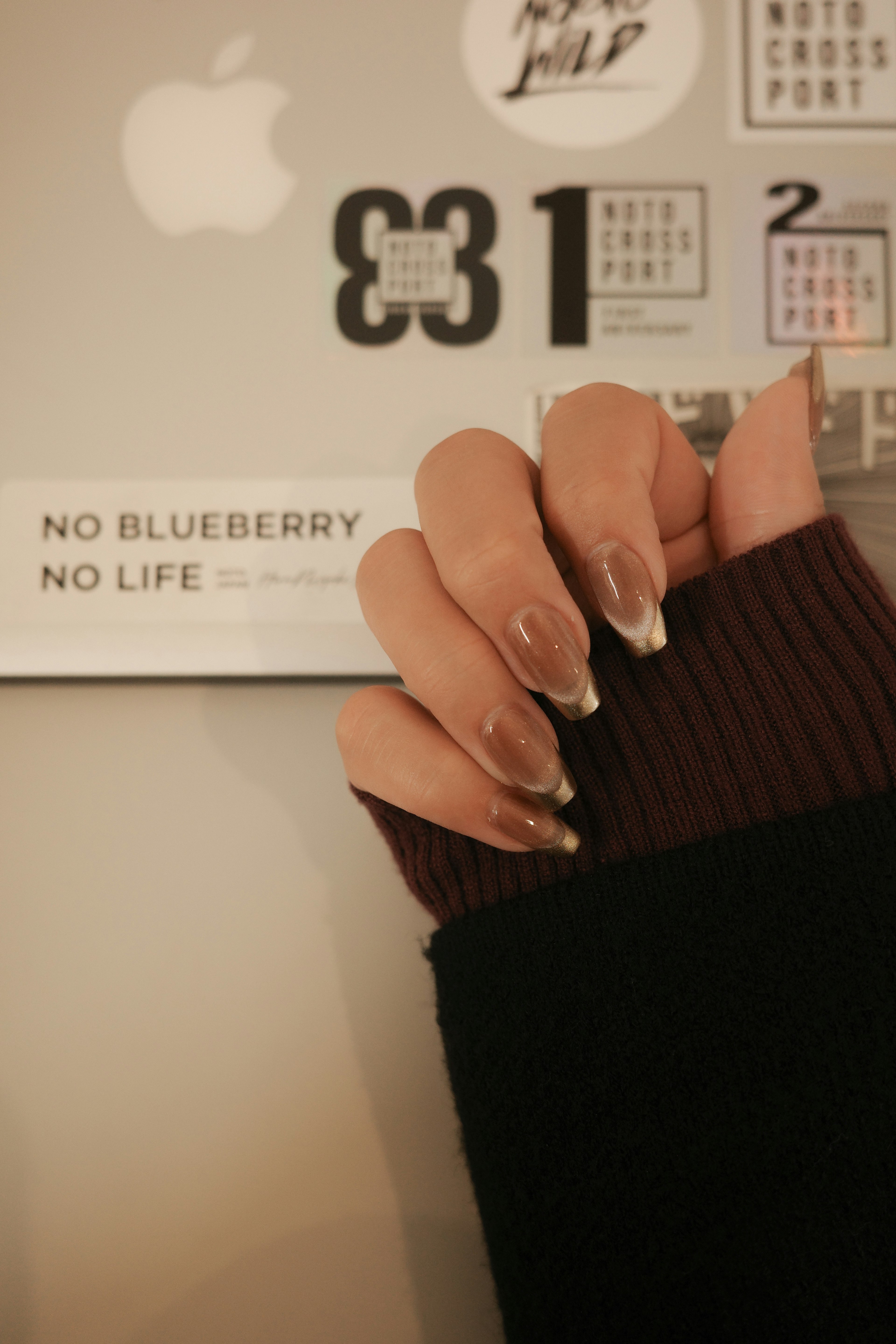 Close-up of a hand with nail art featuring a sweater sleeve and stickers in the background