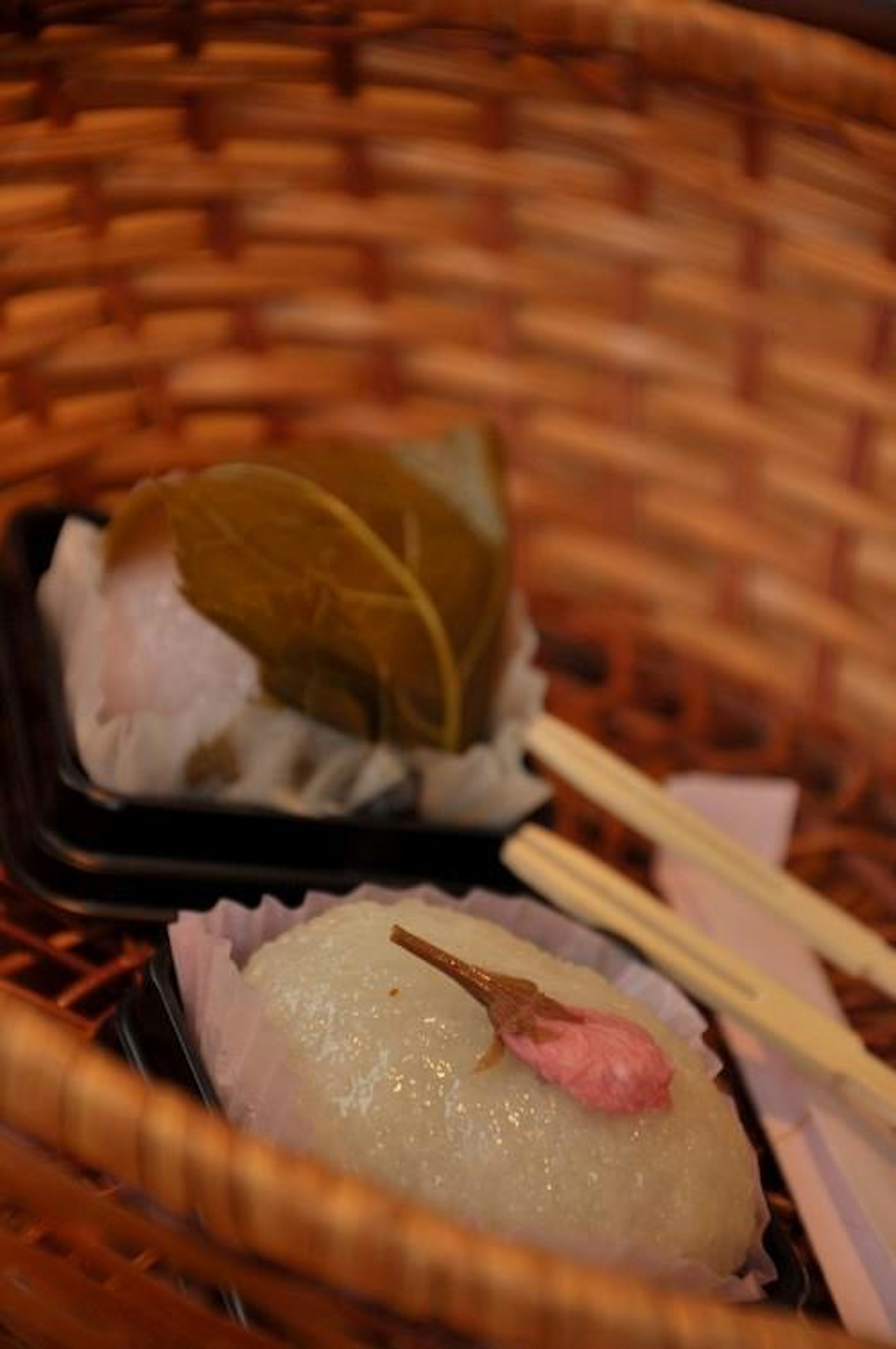 Ein geflochtener Korb mit Sakura-Mochi und einer in einem Blatt gewickelten japanischen Süßigkeit