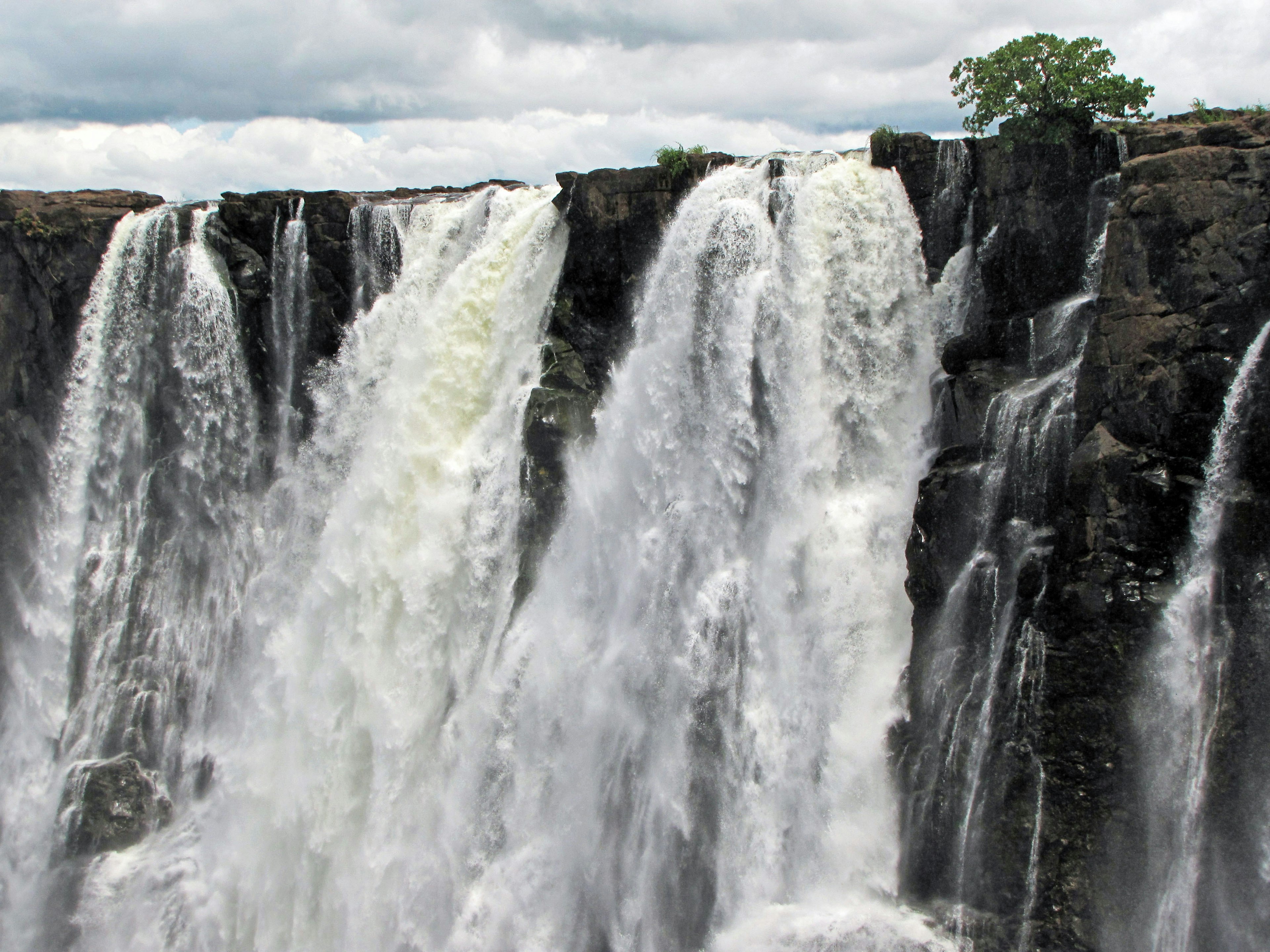 Air terjun yang kuat mengalir di atas tebing berbatu dengan vegetasi yang subur