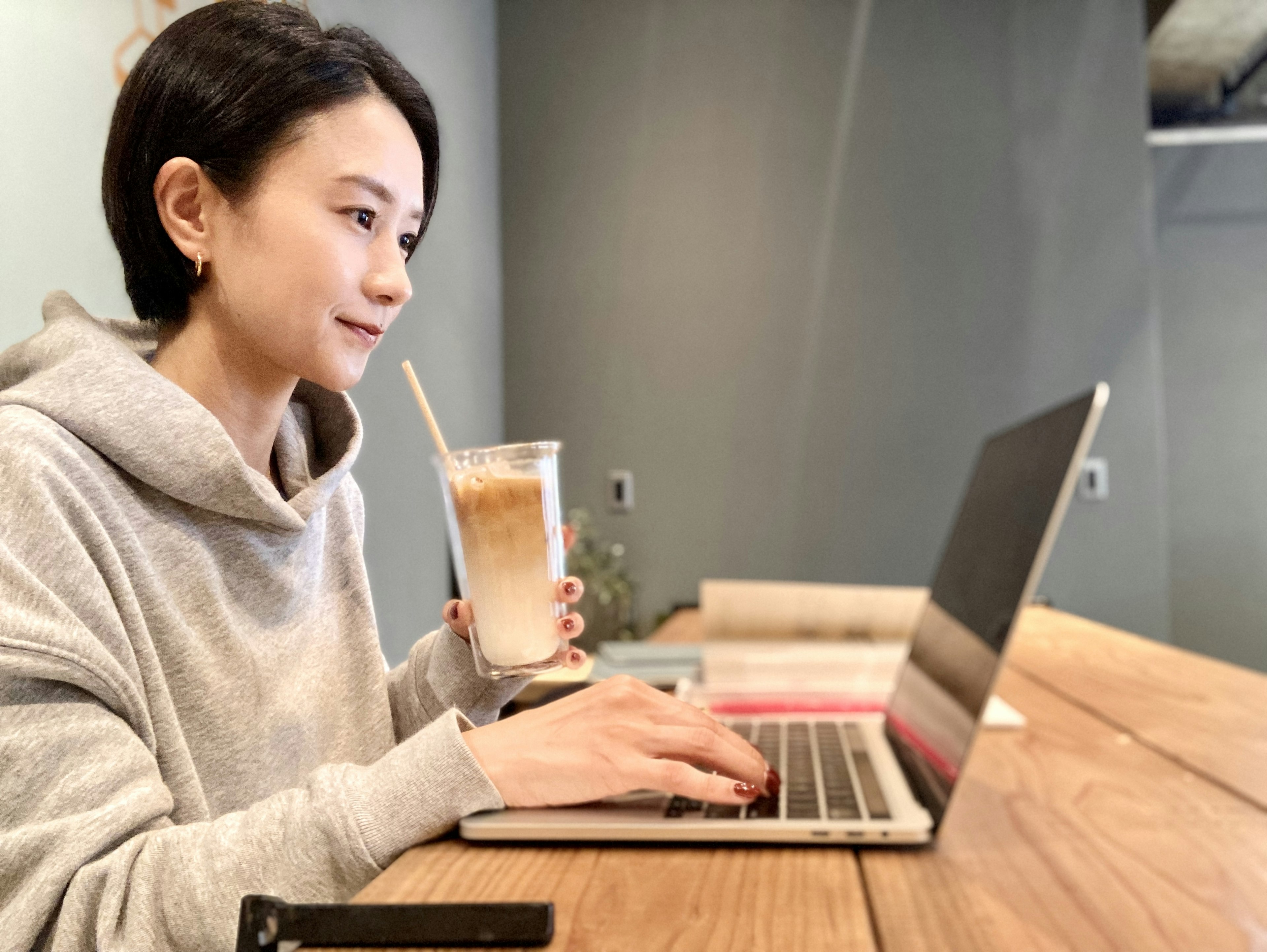 女性がパソコンで作業しながら飲み物を持っているカフェのシーン