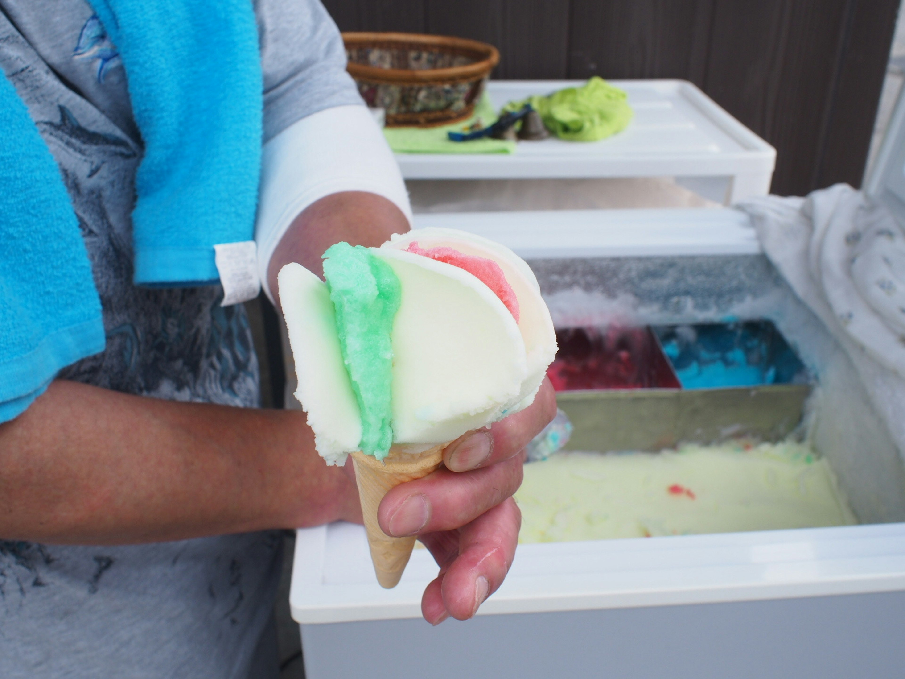 Mano sosteniendo un cono de helado con bolas coloridas en un congelador