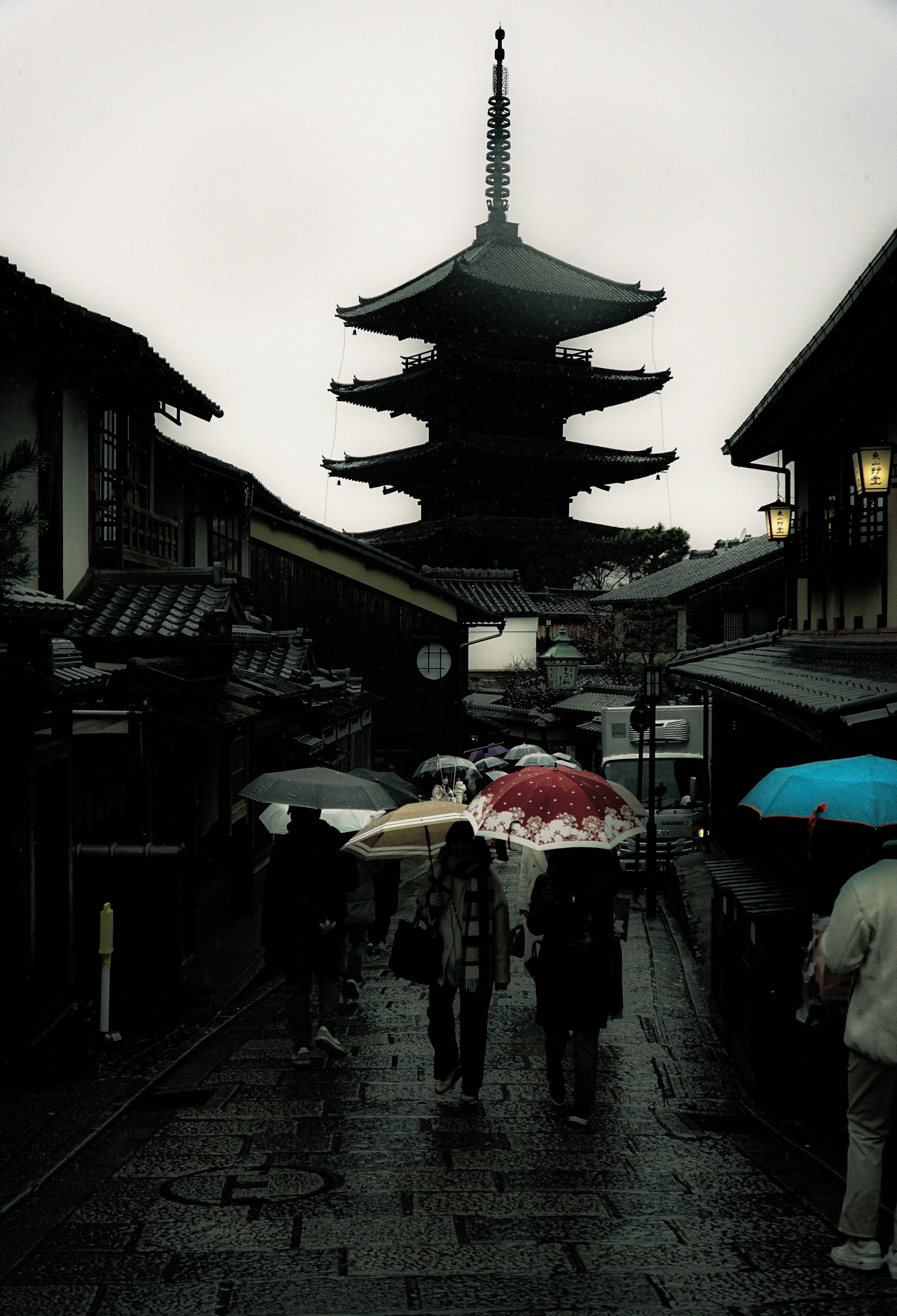 Silhouette di persone con ombrelli di fronte a una pagoda sotto la pioggia