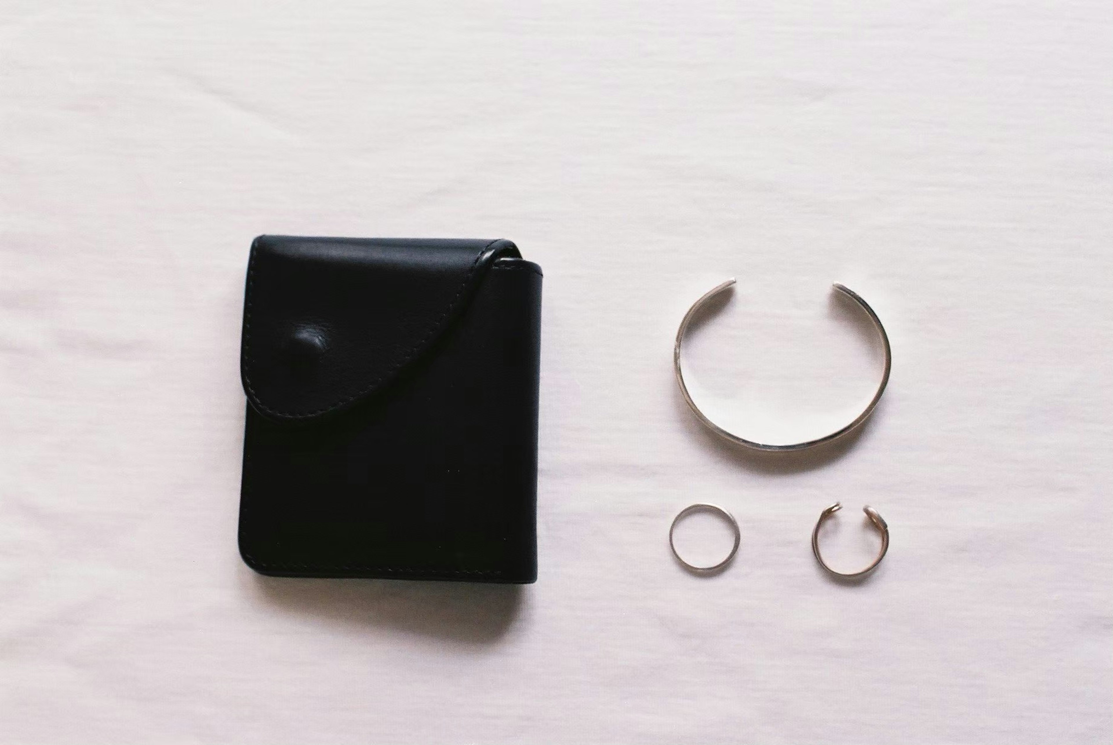 A black leather wallet and silver jewelry arranged on a white background