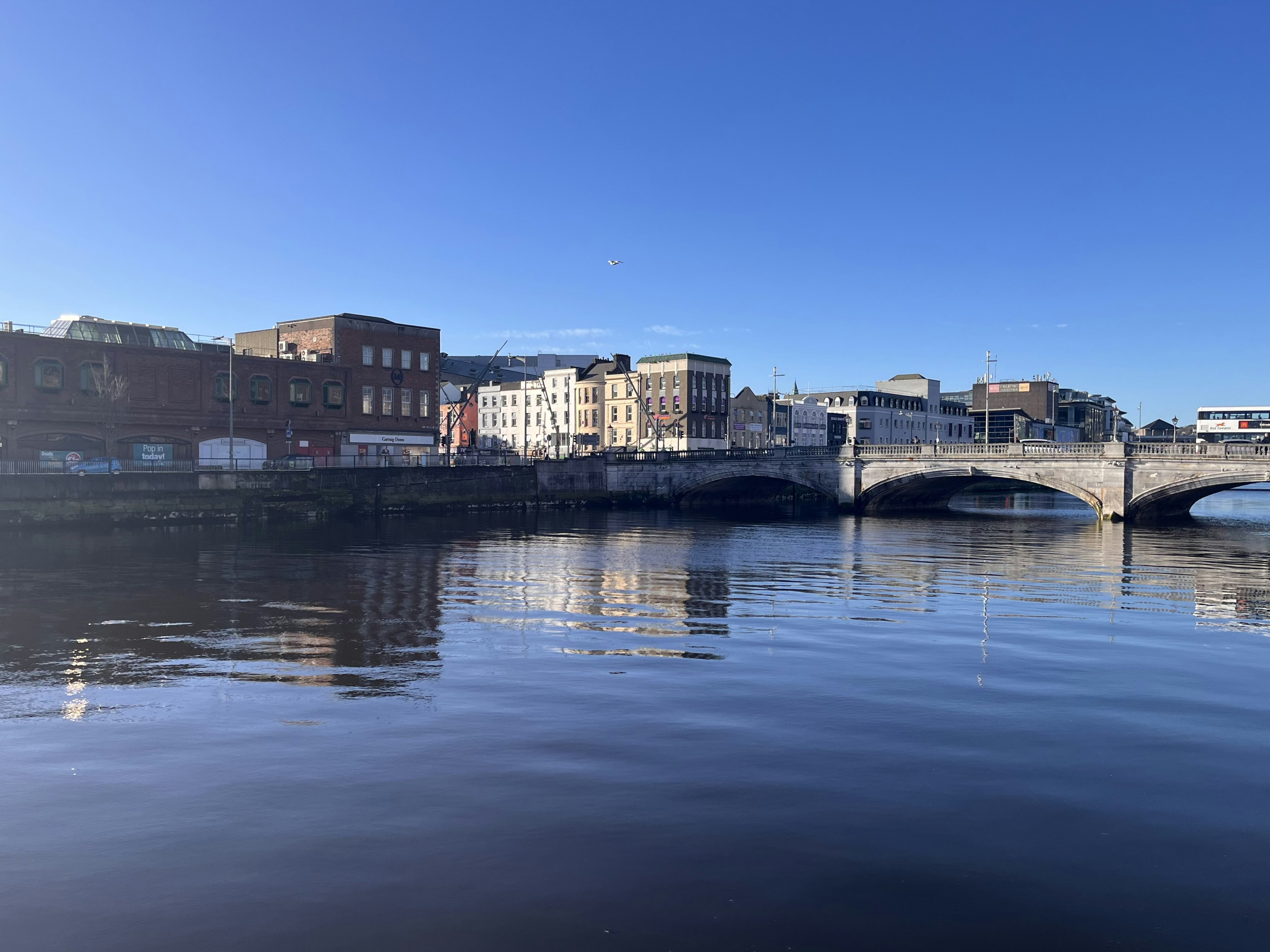 Paesaggio urbano dell'Irlanda con edifici e un ponte che si riflettono nel fiume sotto un cielo sereno