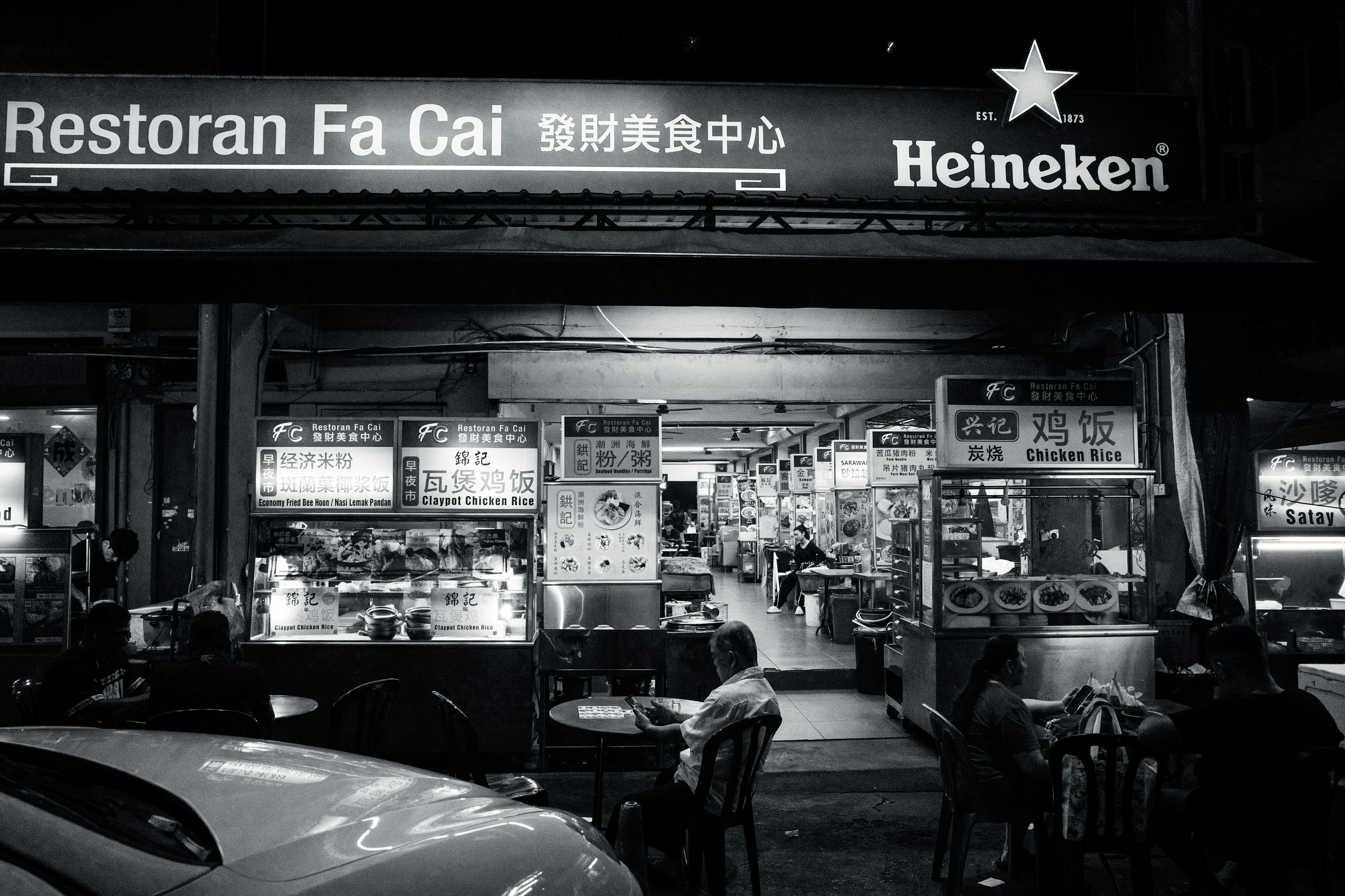 Vue nocturne du Restoran Fa Cai avec des stands de nourriture et une enseigne Heineken