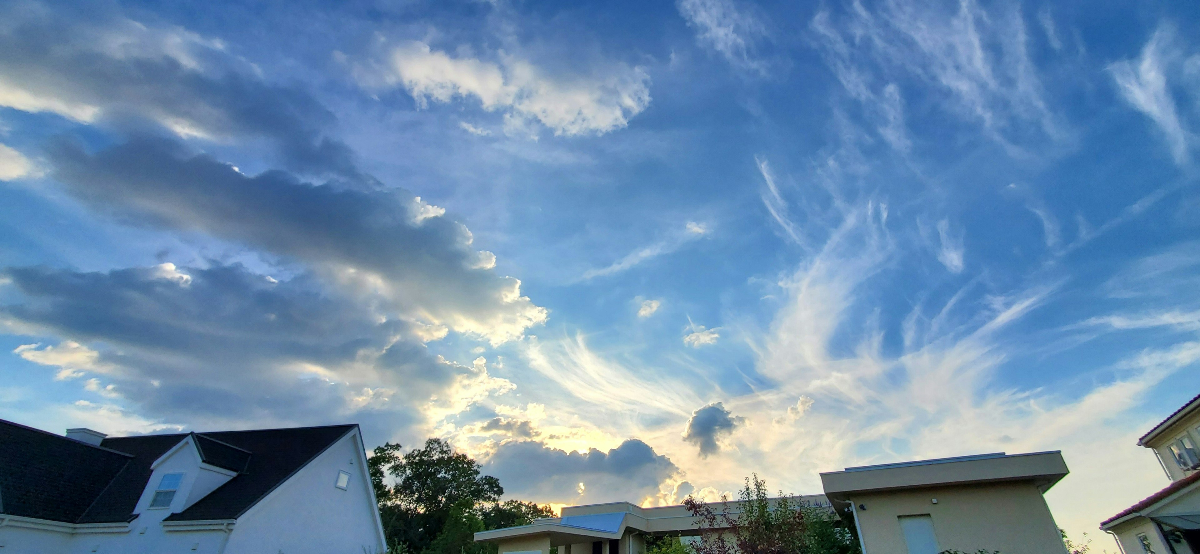 Panoramic view of a blue sky with wispy clouds and silhouettes of houses