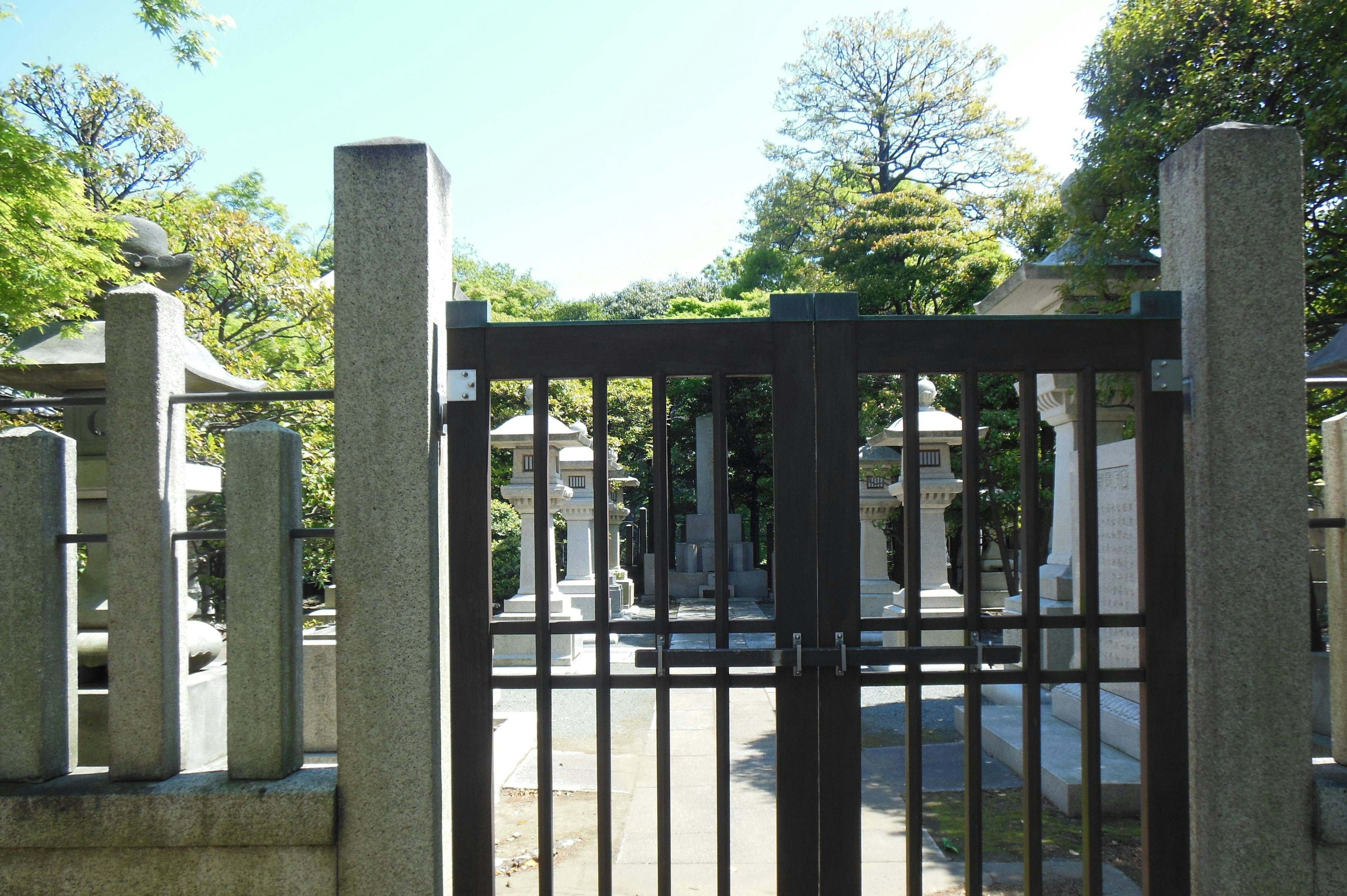 View of an open gate to a serene cemetery surrounded by lush trees and stone tombs