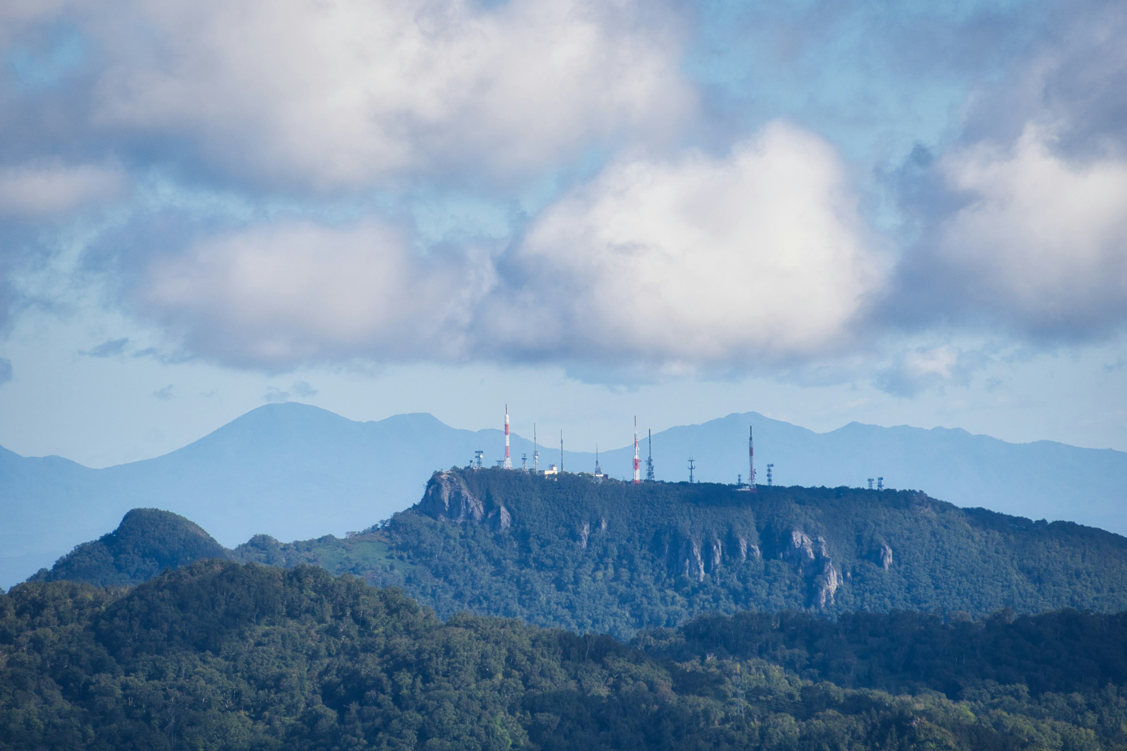 Paysage de montagne sous un ciel bleu avec des nuages et des tours de communication au sommet