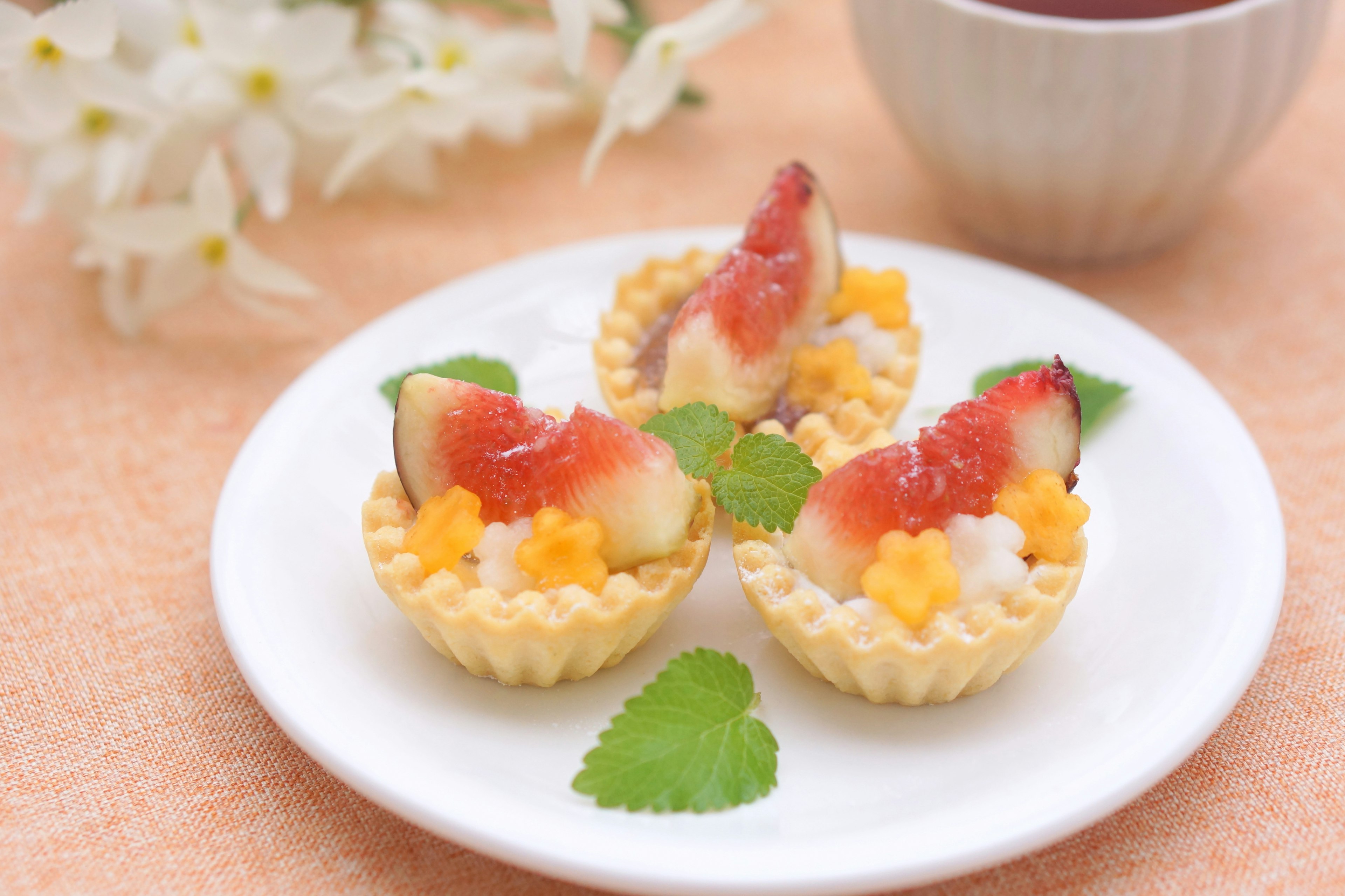 Small fruit tarts arranged on a plate with a cup of tea