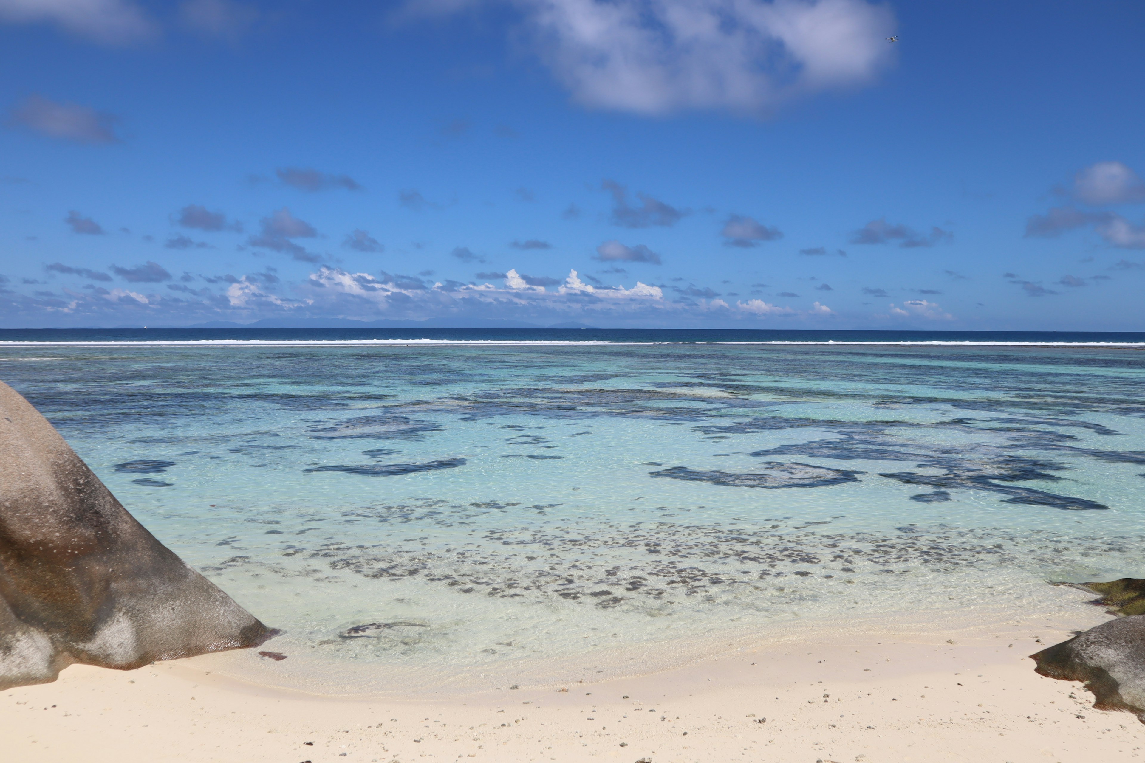 Beautiful landscape featuring blue ocean and white sandy beach with large rock and clear water