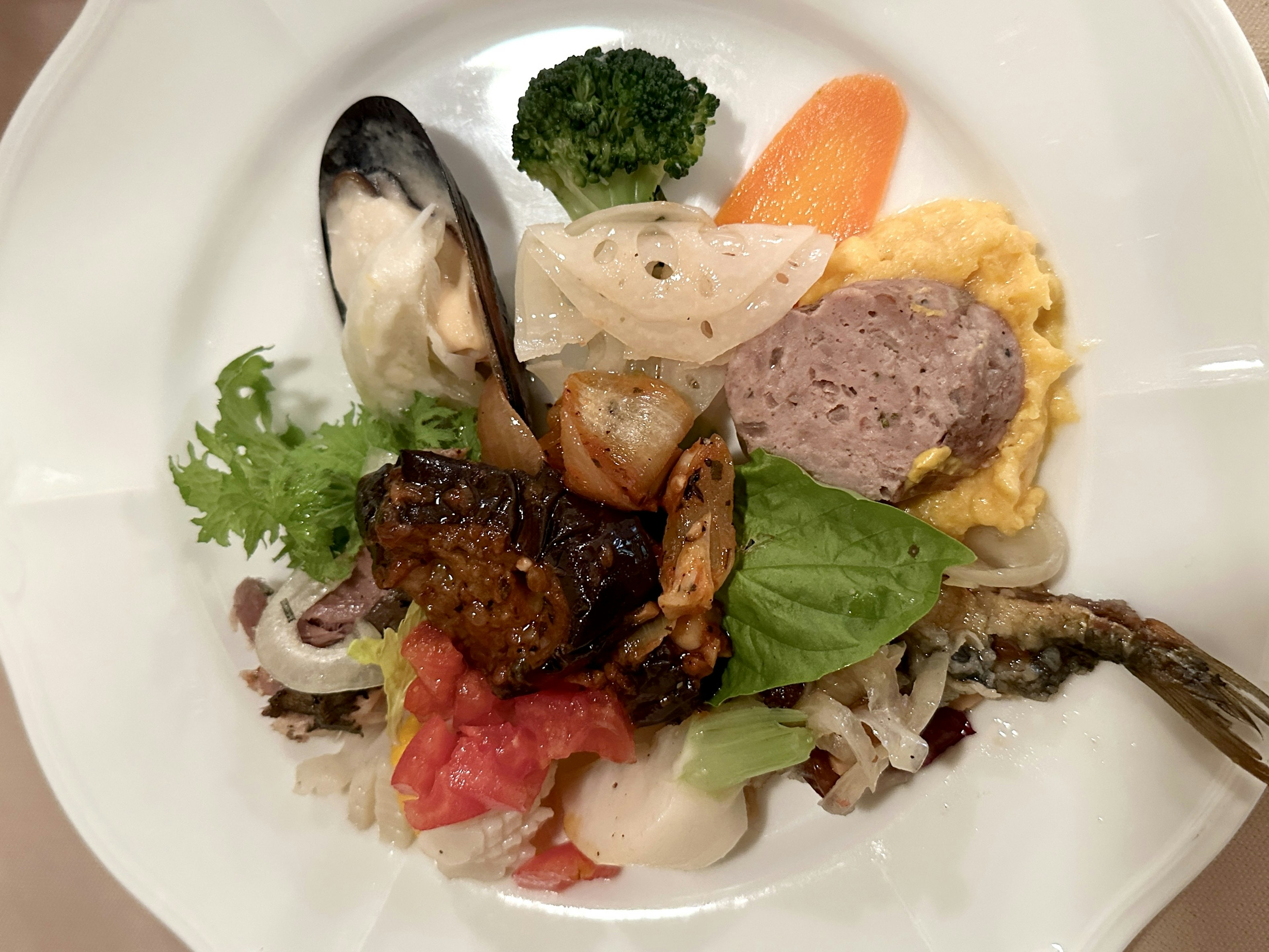 A plate featuring a variety of dishes including mussels, shrimp, omelet, and vegetables