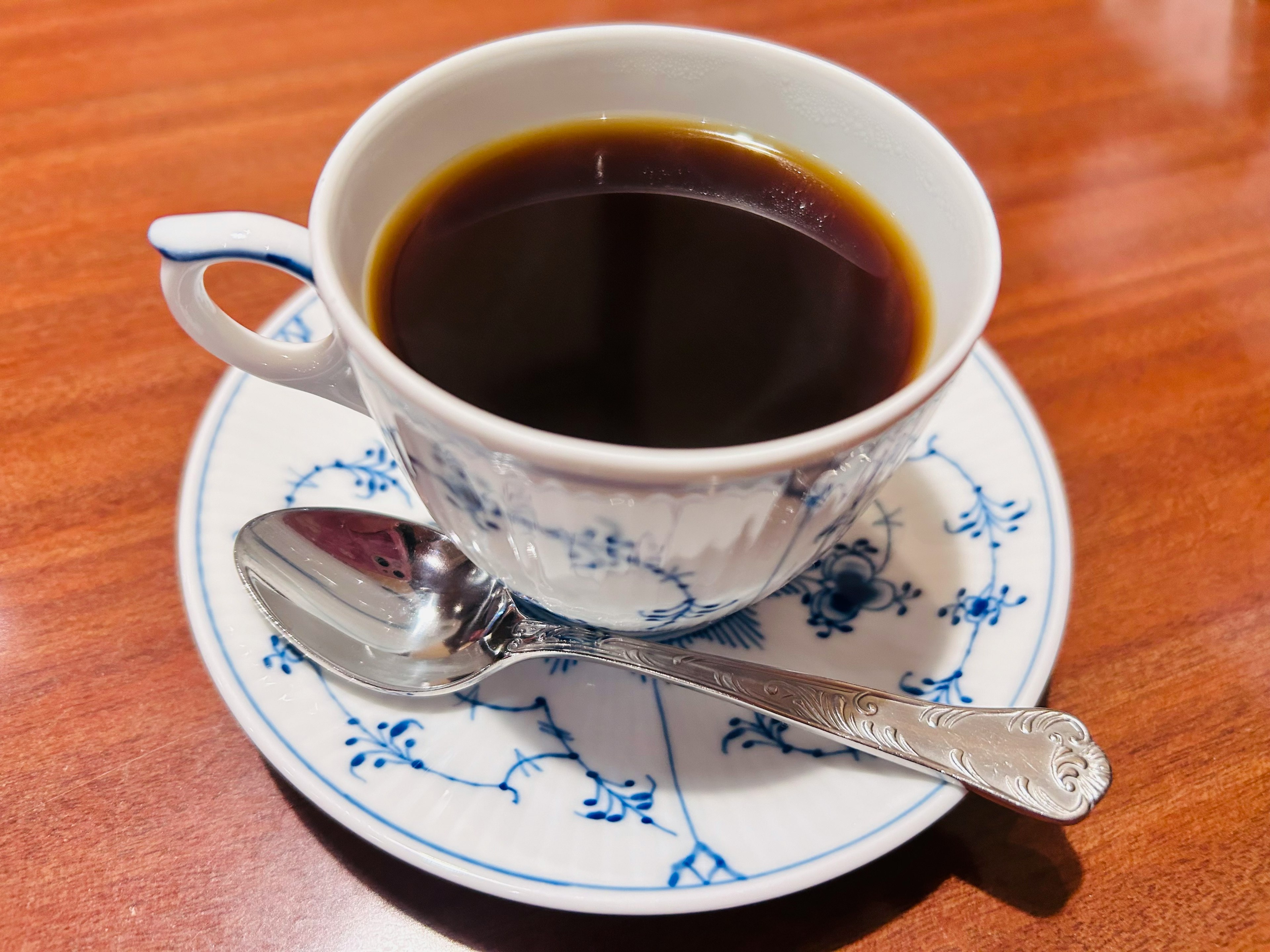 Caffè nero in una tazza con motivo floreale blu e un cucchiaio