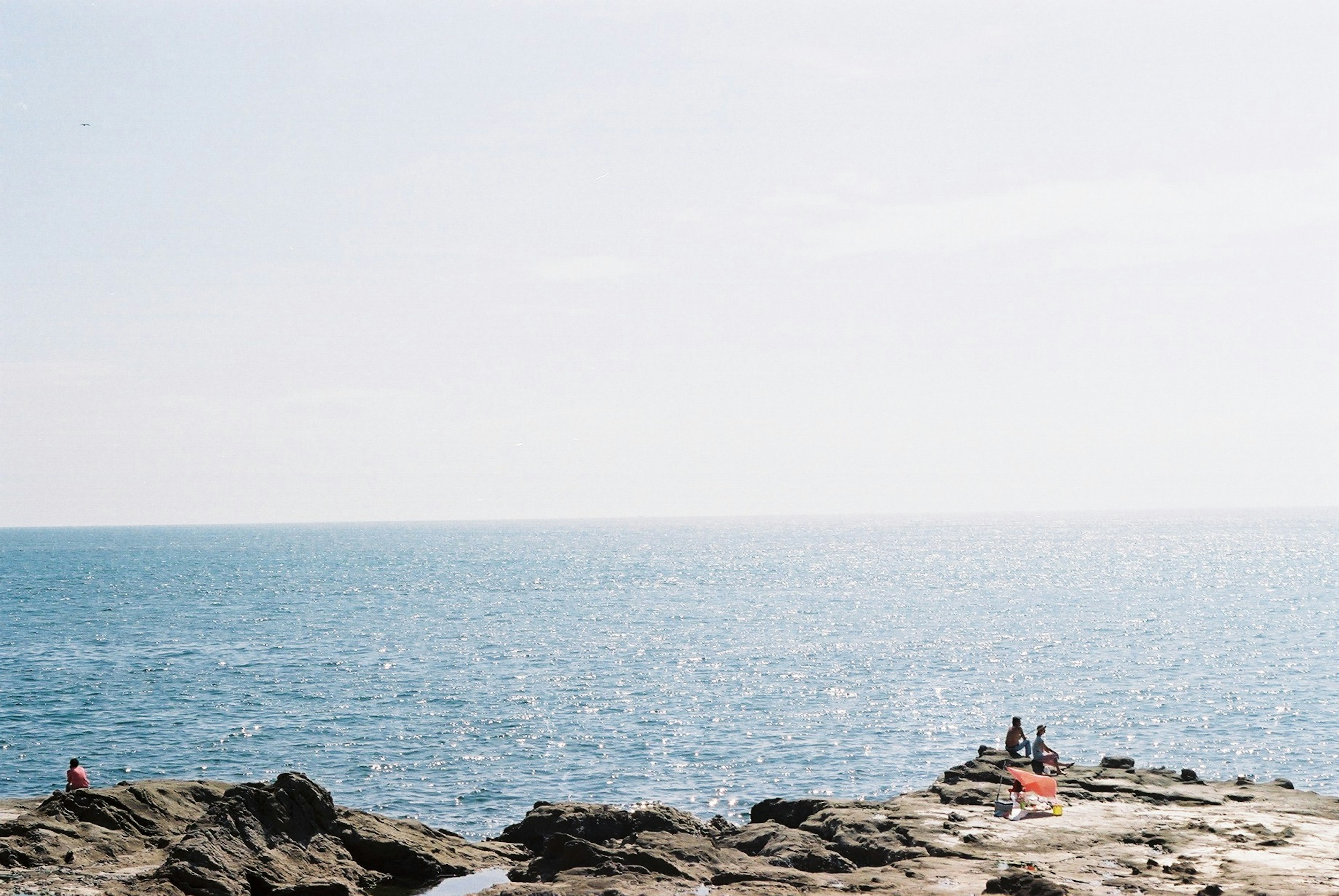 A scenic view of people enjoying the blue sea and rocky shore