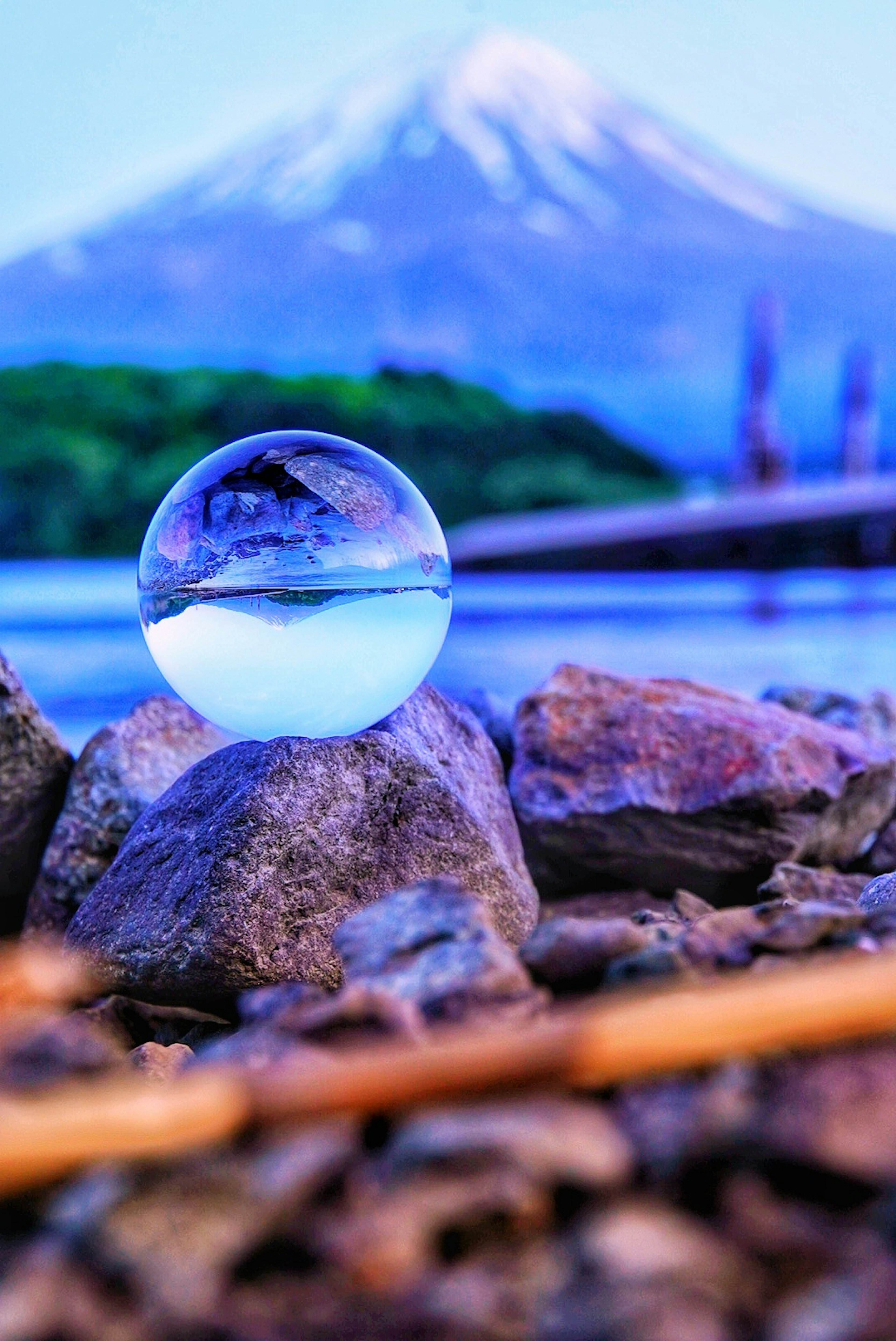 A transparent sphere reflecting water sits on rocks with a snow-capped mountain in the background