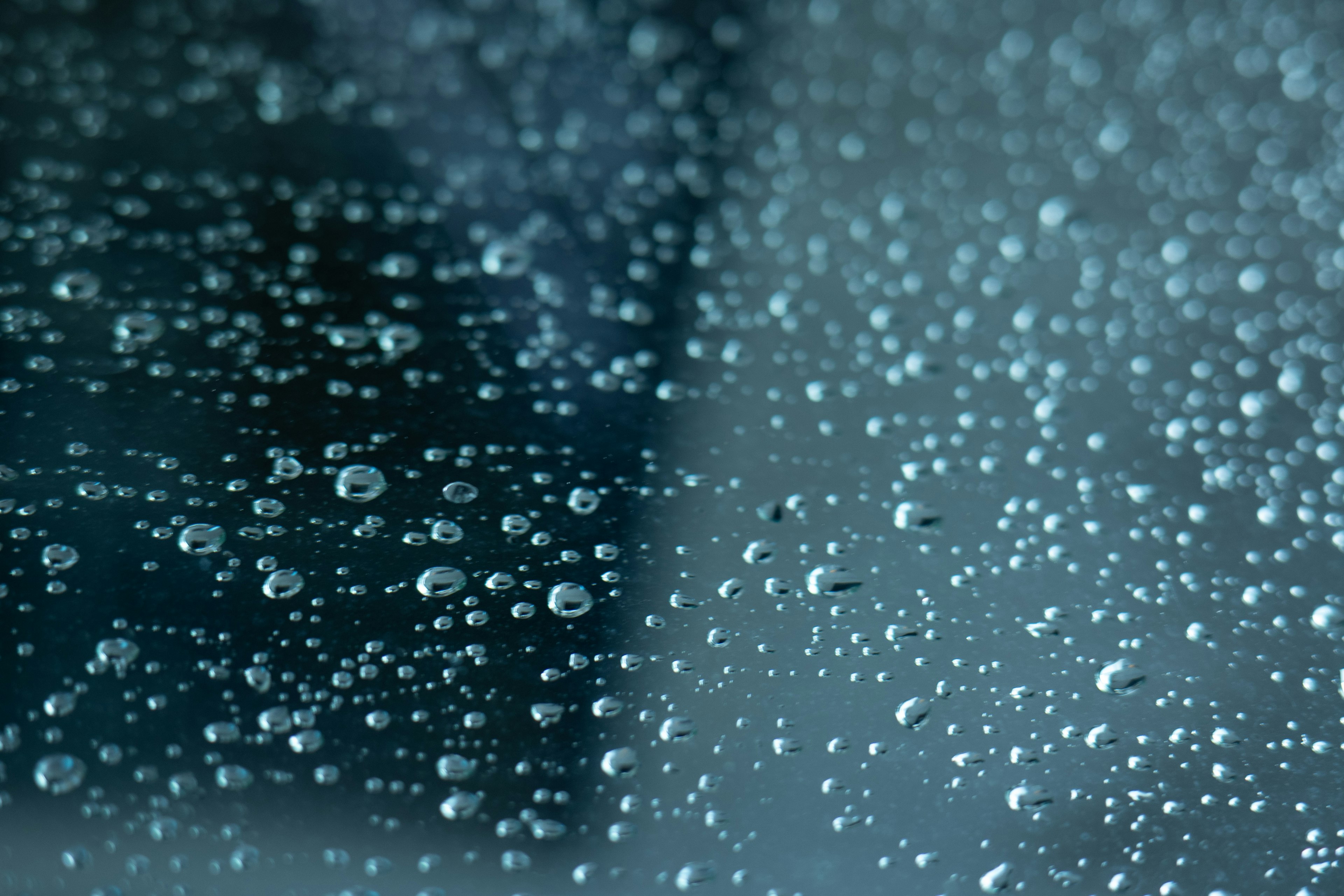 Close-up of water droplets on glass with a bluish green background