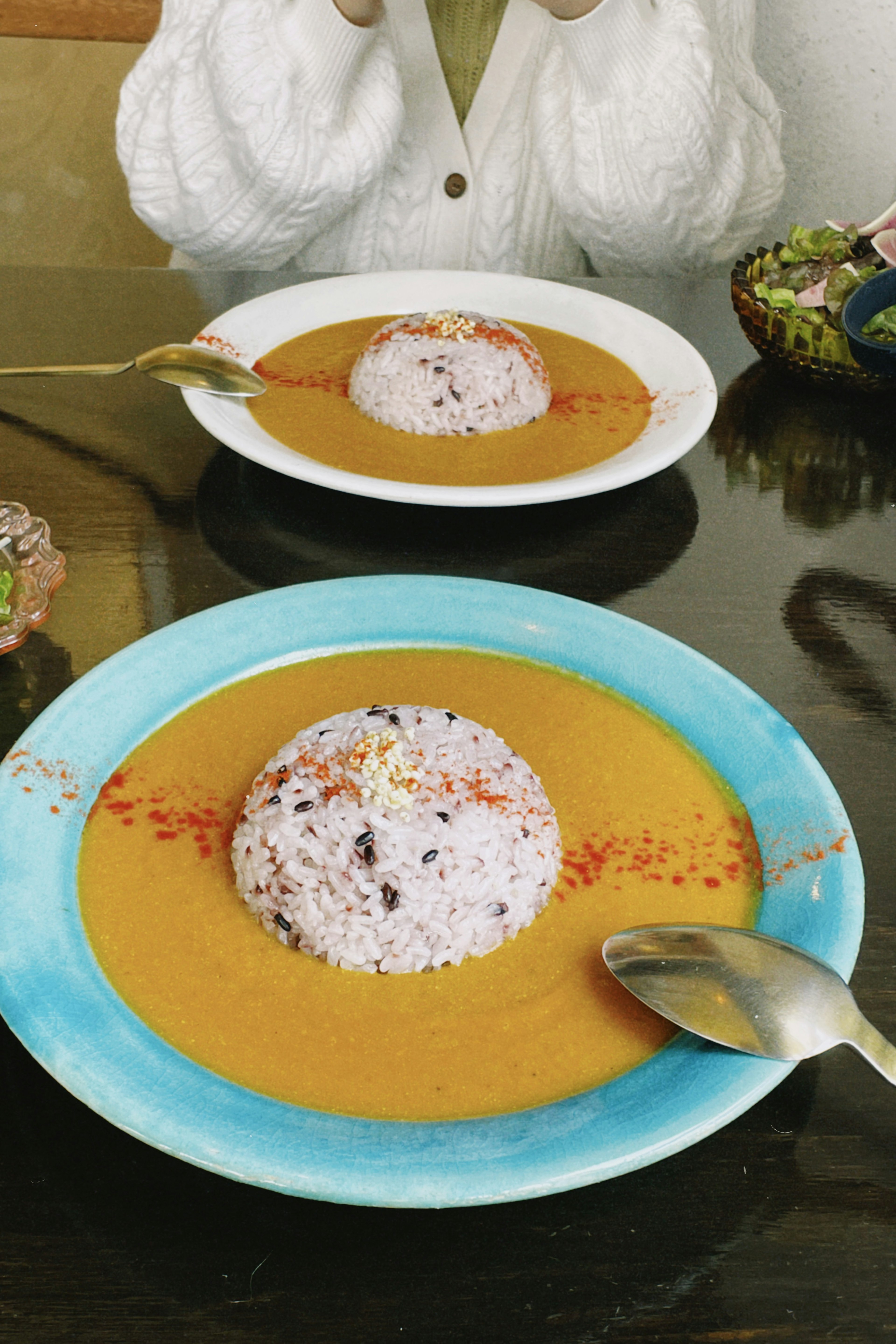 Dua piring kari dengan nasi dalam piring biru dan putih cerah dengan tumpukan nasi yang dihiasi dengan rempah merah