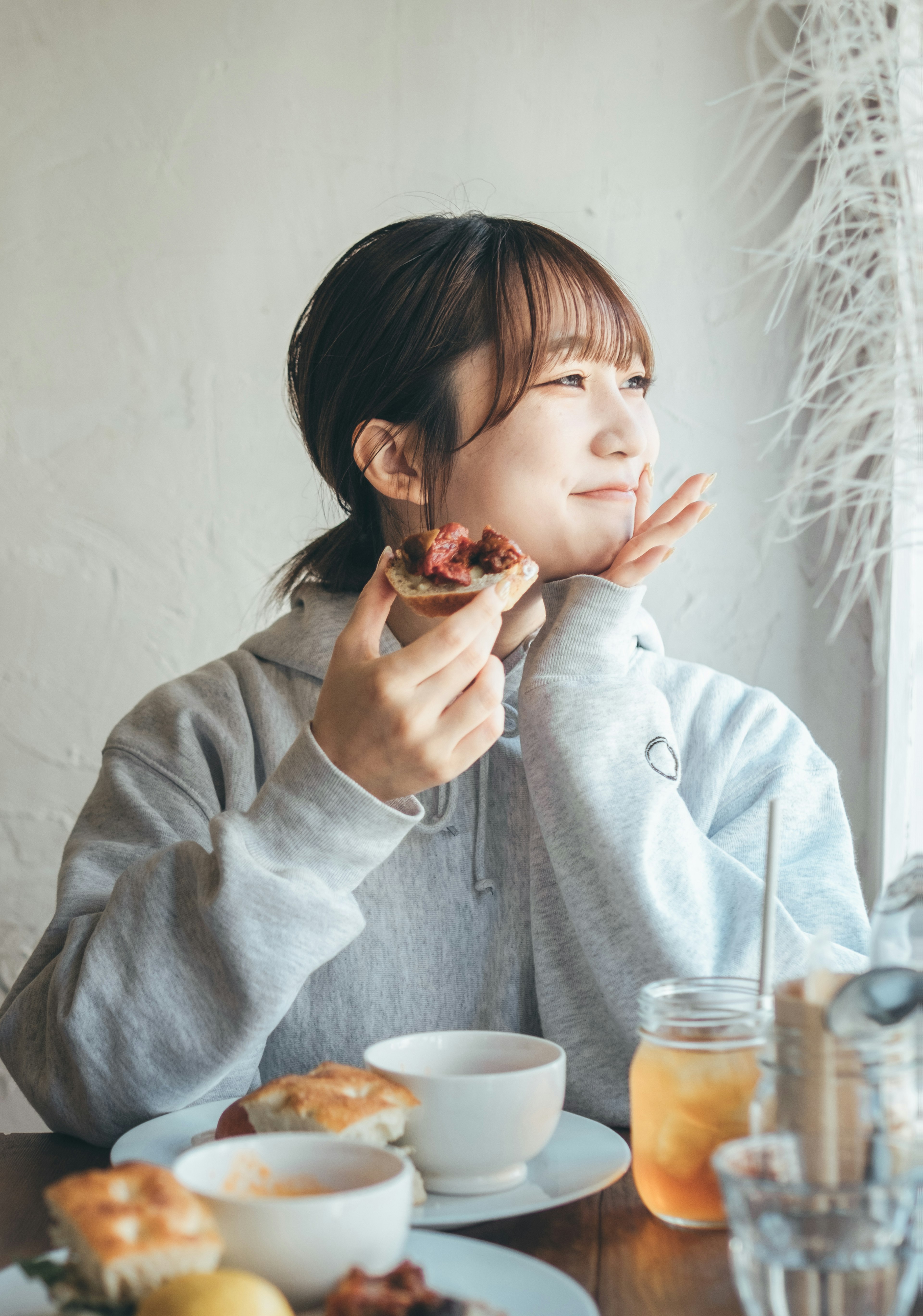 窓際で食事を楽しむ女性が笑顔で食べ物を手に持ちポーズをとっている