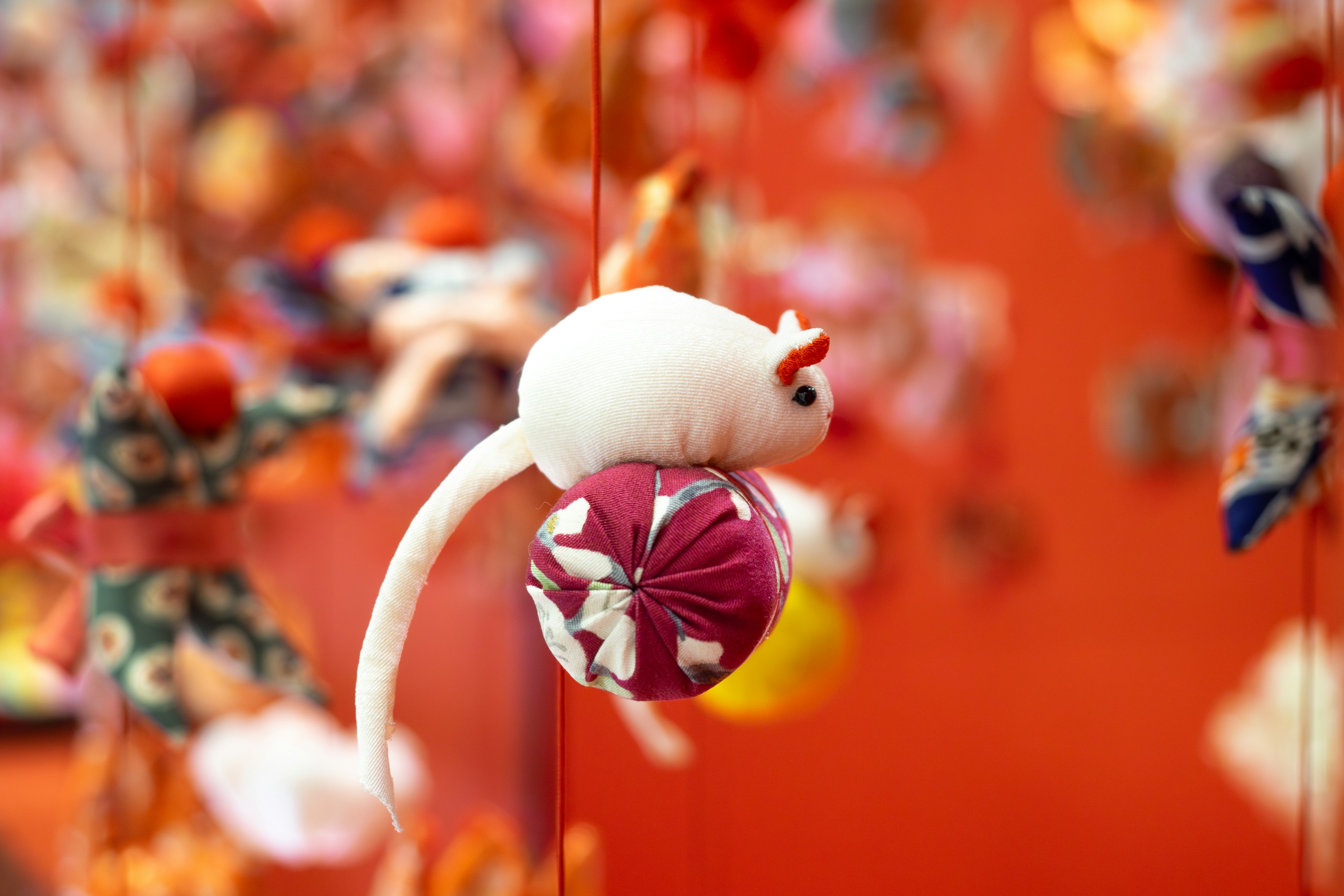 A white mouse plush sitting on a purple ball in front of colorful decorations