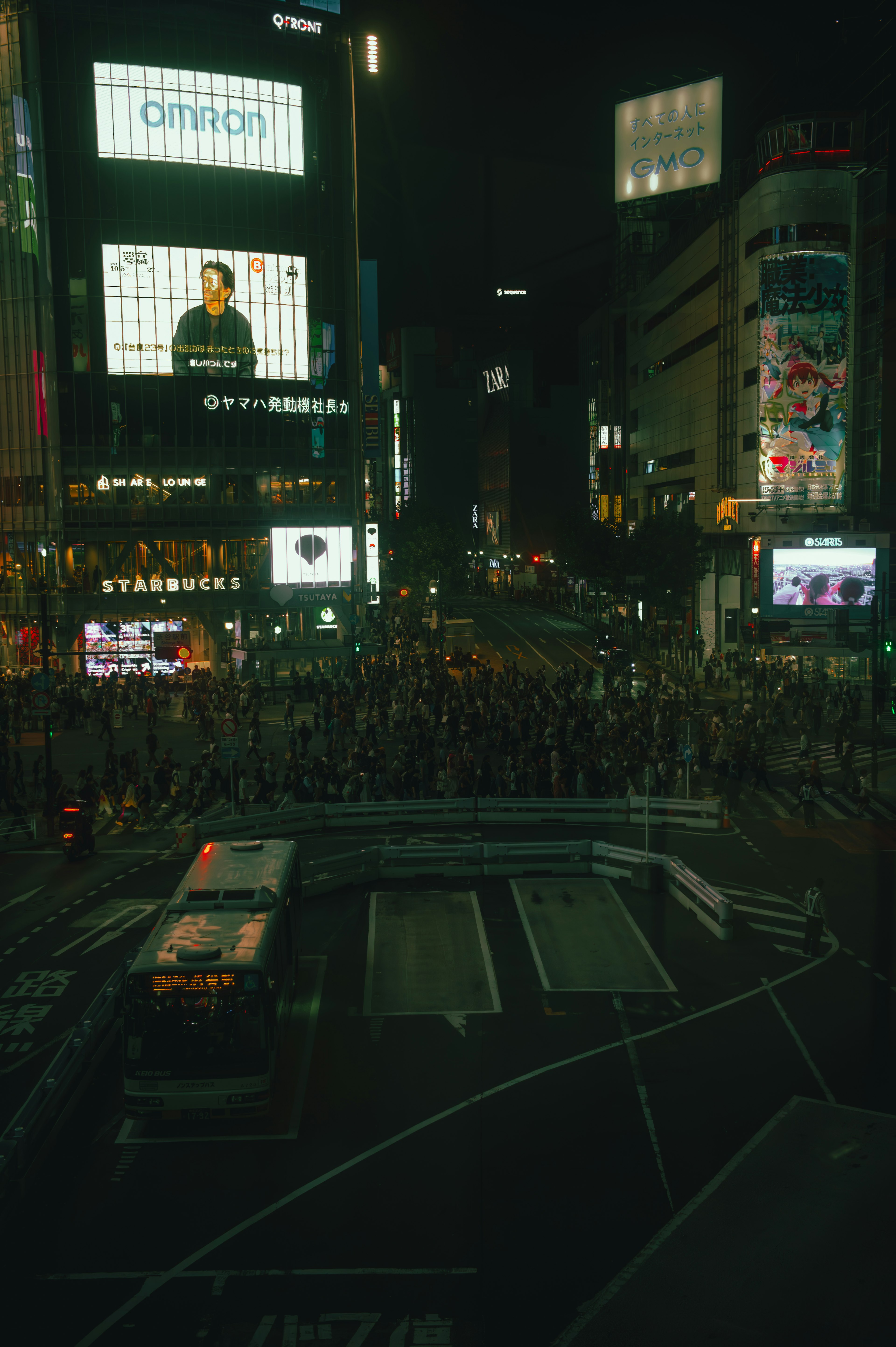 Kerumunan di persimpangan Shibuya dengan papan iklan besar di malam hari