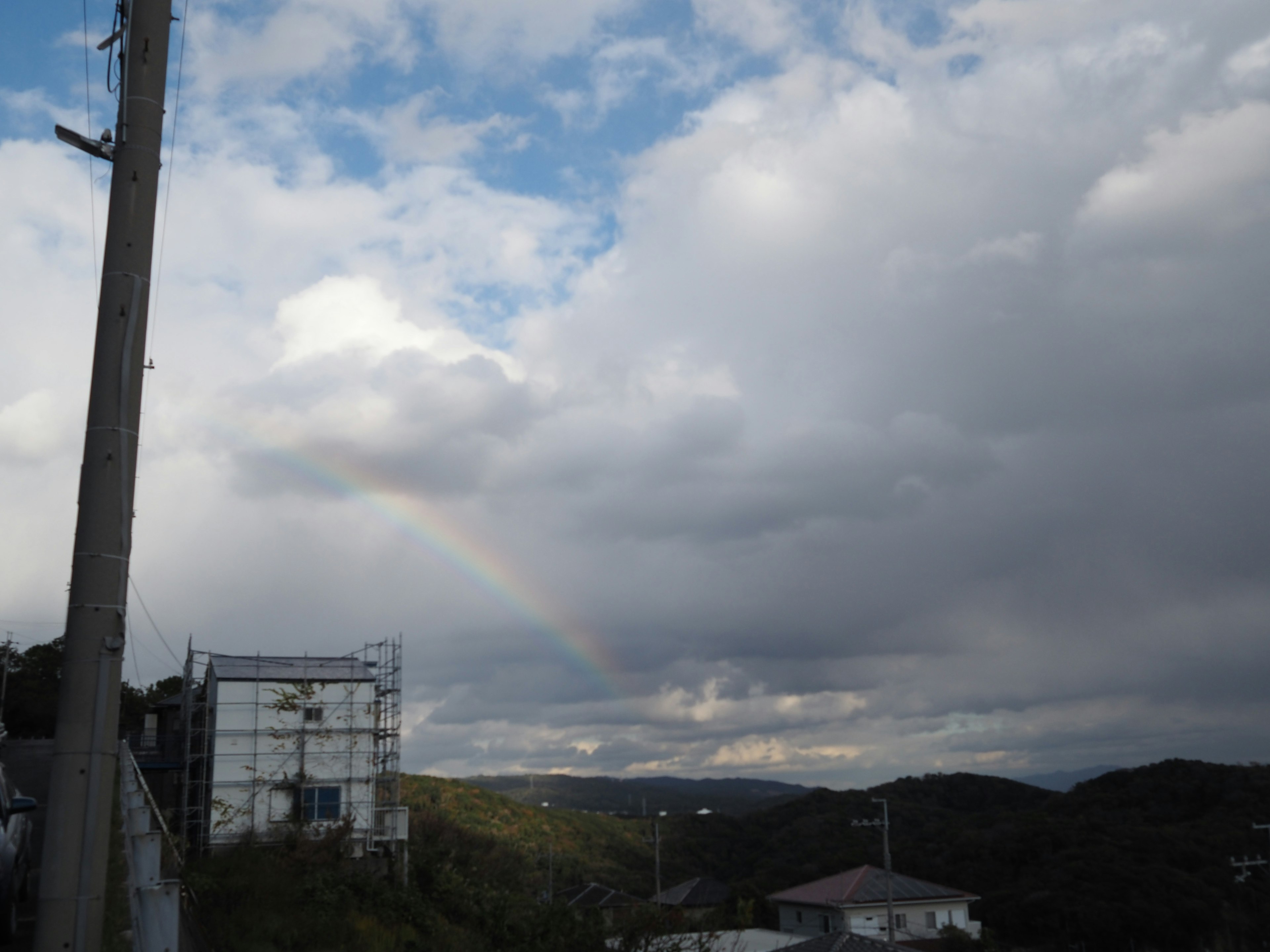 Pelangi melengkung di atas langit yang mendung dan perbukitan