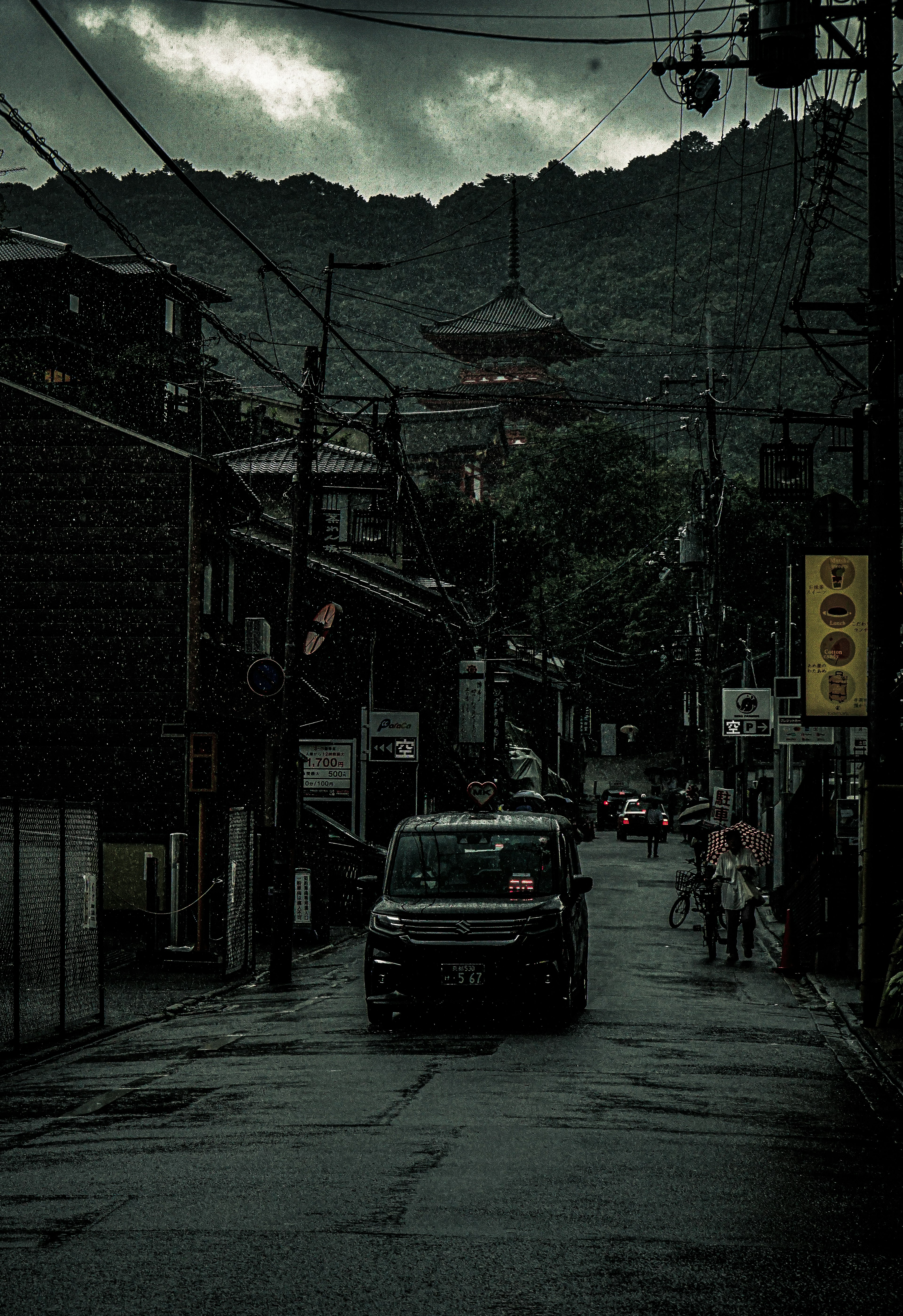 Vista escénica de una calle antigua con un coche que pasa bajo nubes oscuras y una montaña al fondo