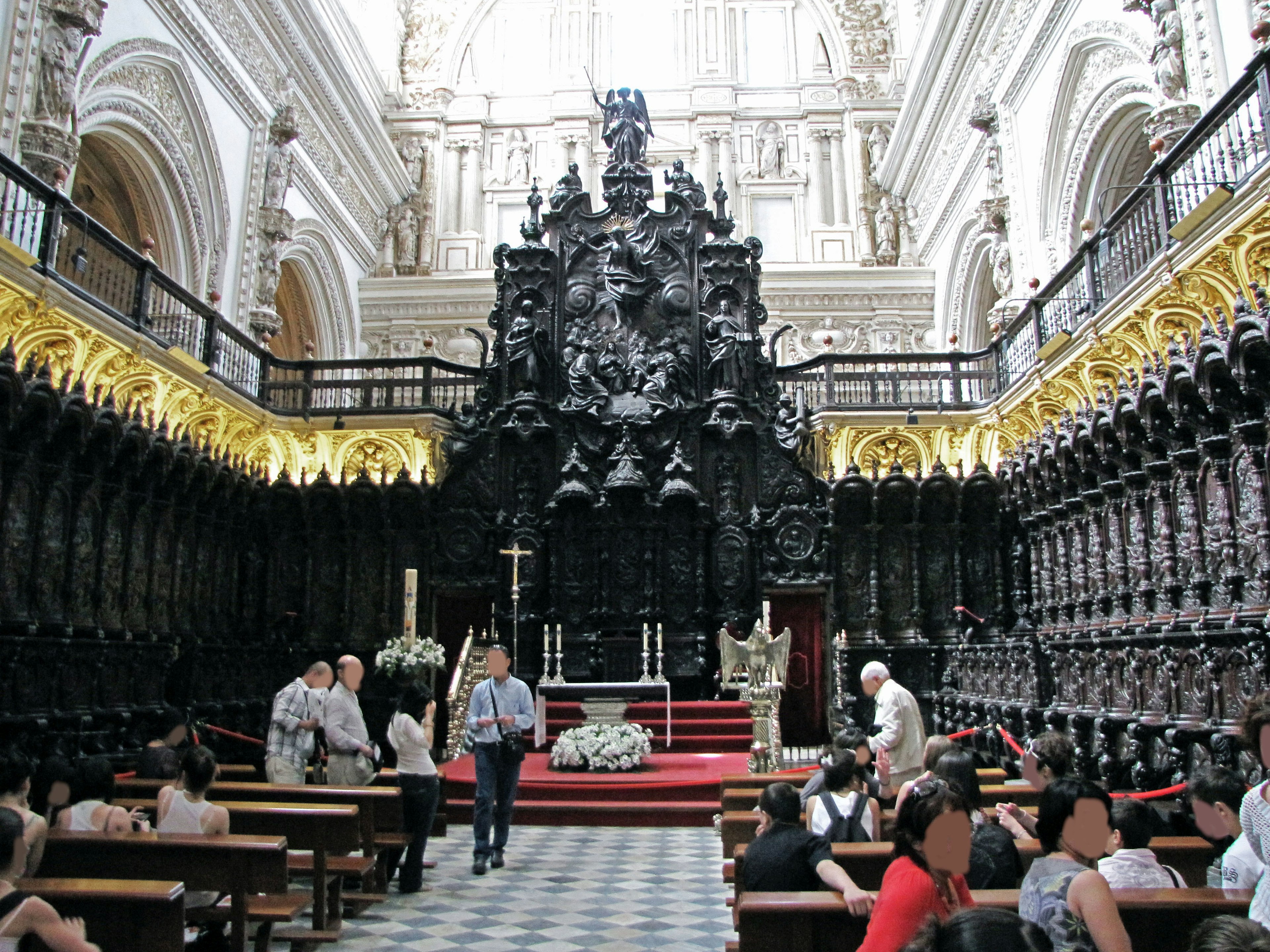 Interior de una iglesia con un grandioso altar esculpido en negro y numerosos visitantes