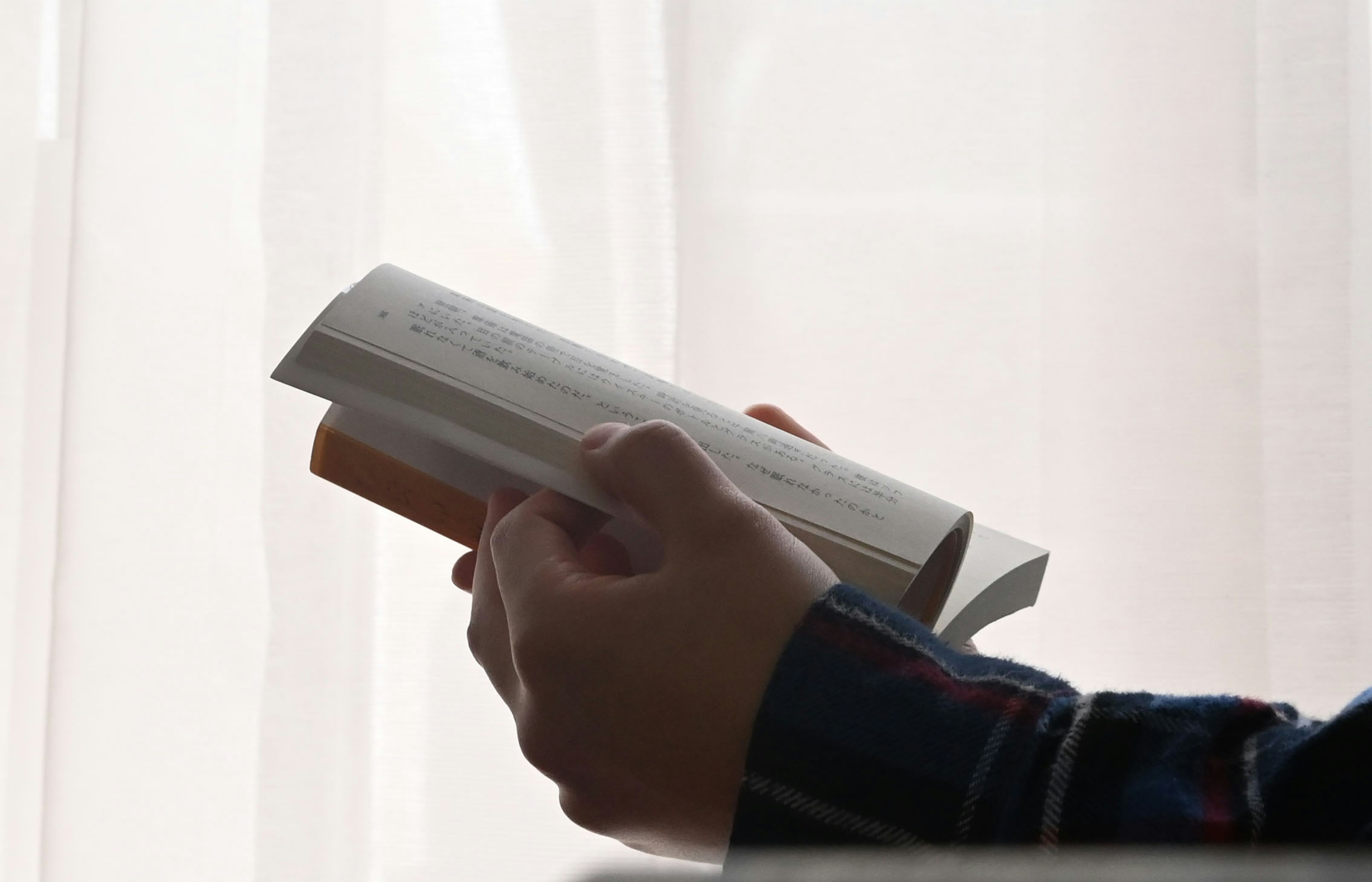 Silhouette de una mano sosteniendo un libro junto a una ventana con luz suave