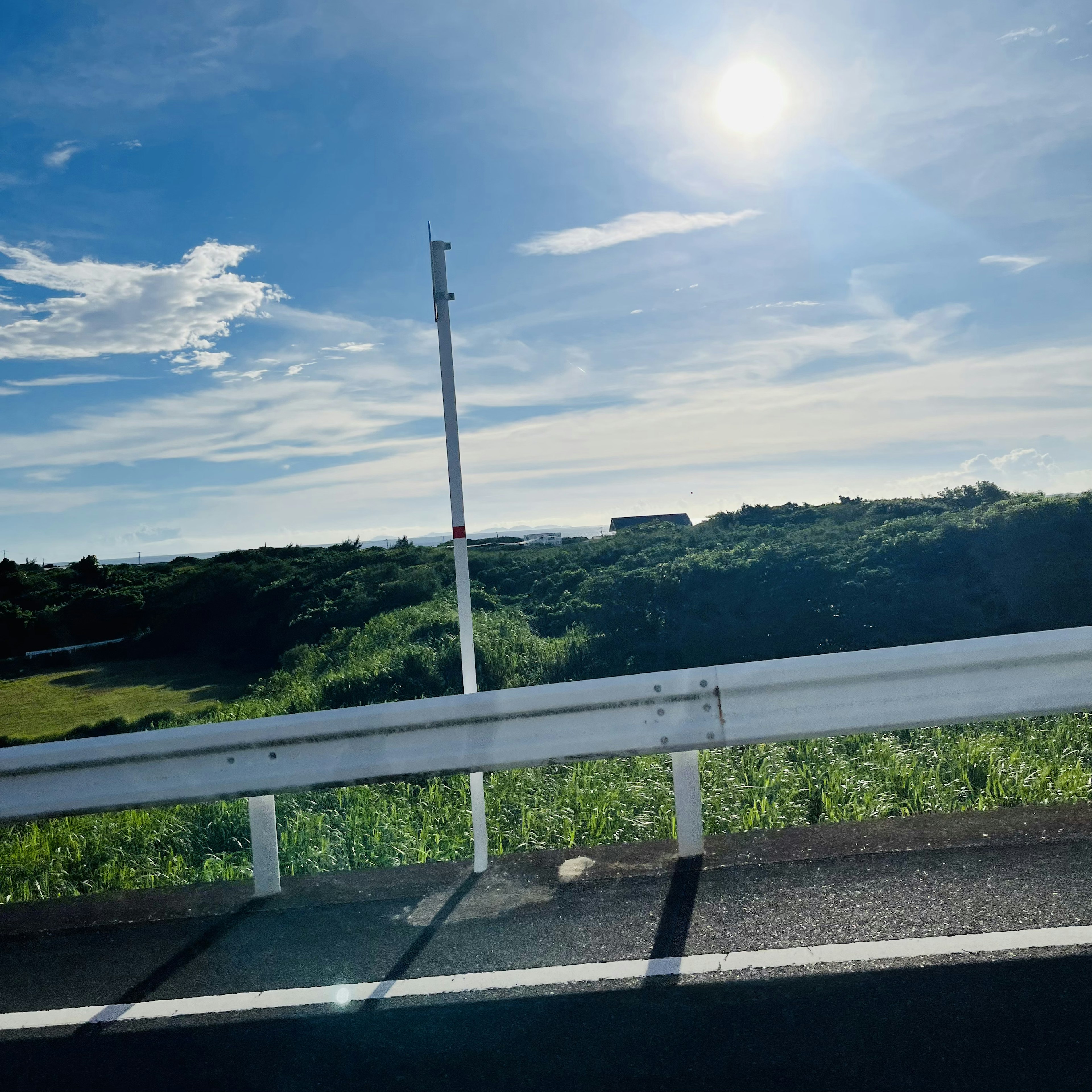 青い空と白い雲が広がる風景 緑の草地と道路の一部 眩しい太陽が輝いている