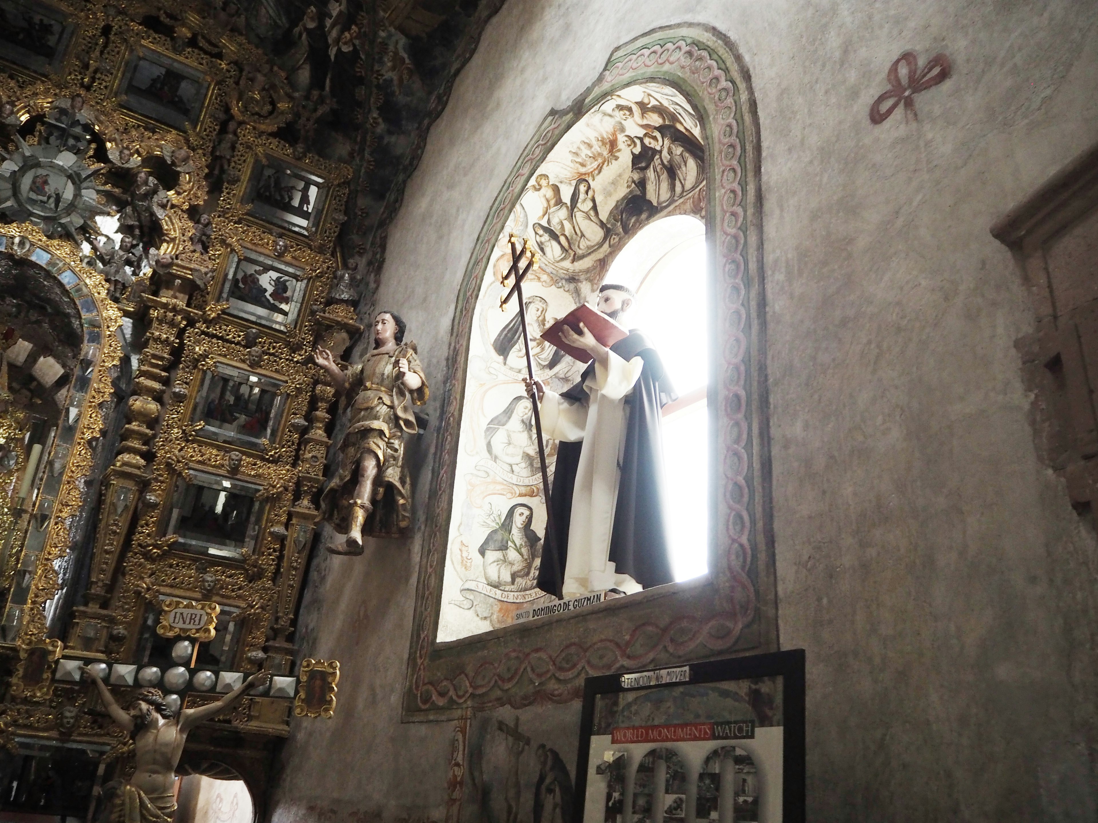 Statua di figura religiosa che si erge in una grande finestra con decorazioni murali ornate e sculture