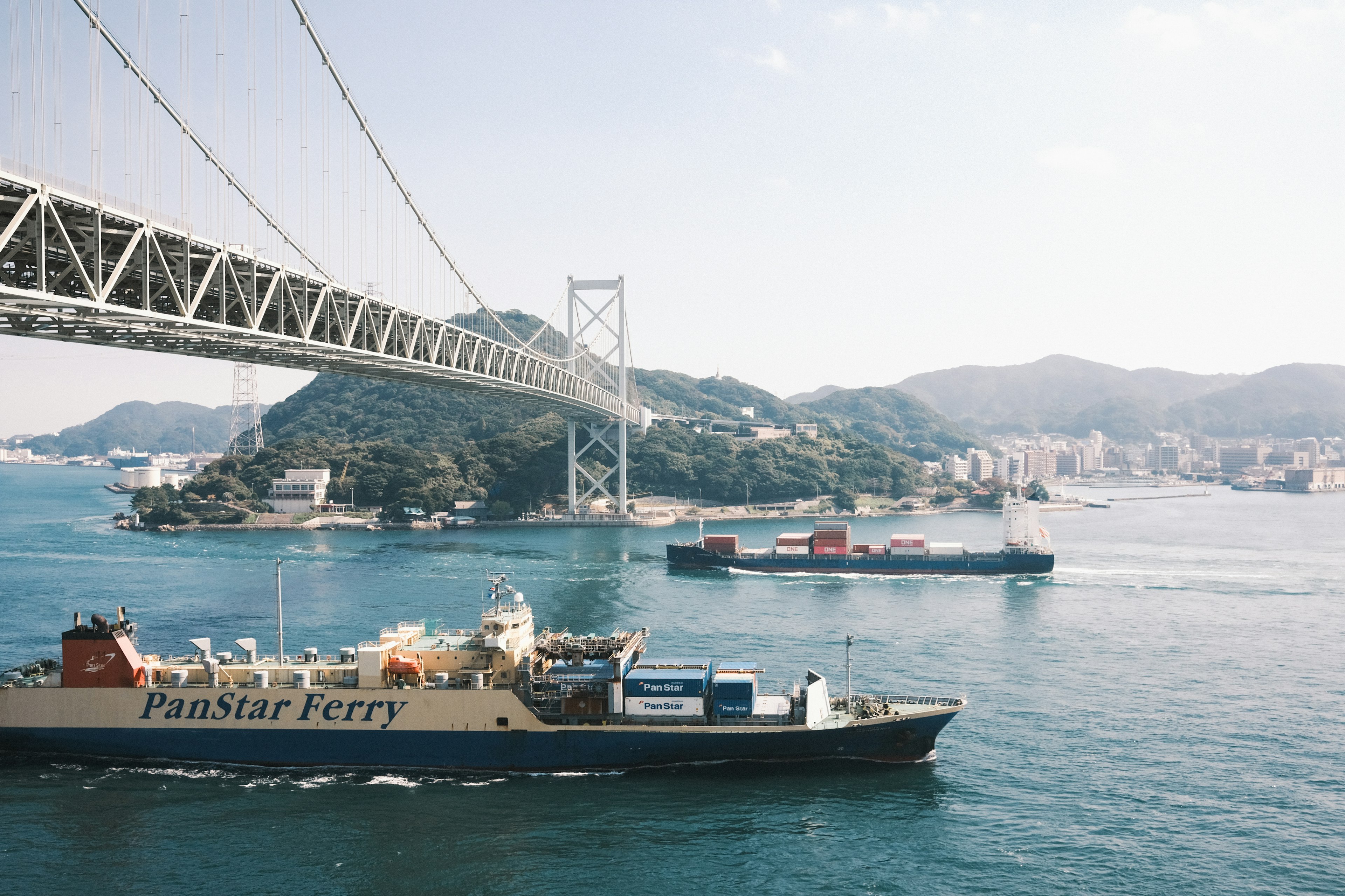 Ferry and cargo ship passing under a bridge over blue waters