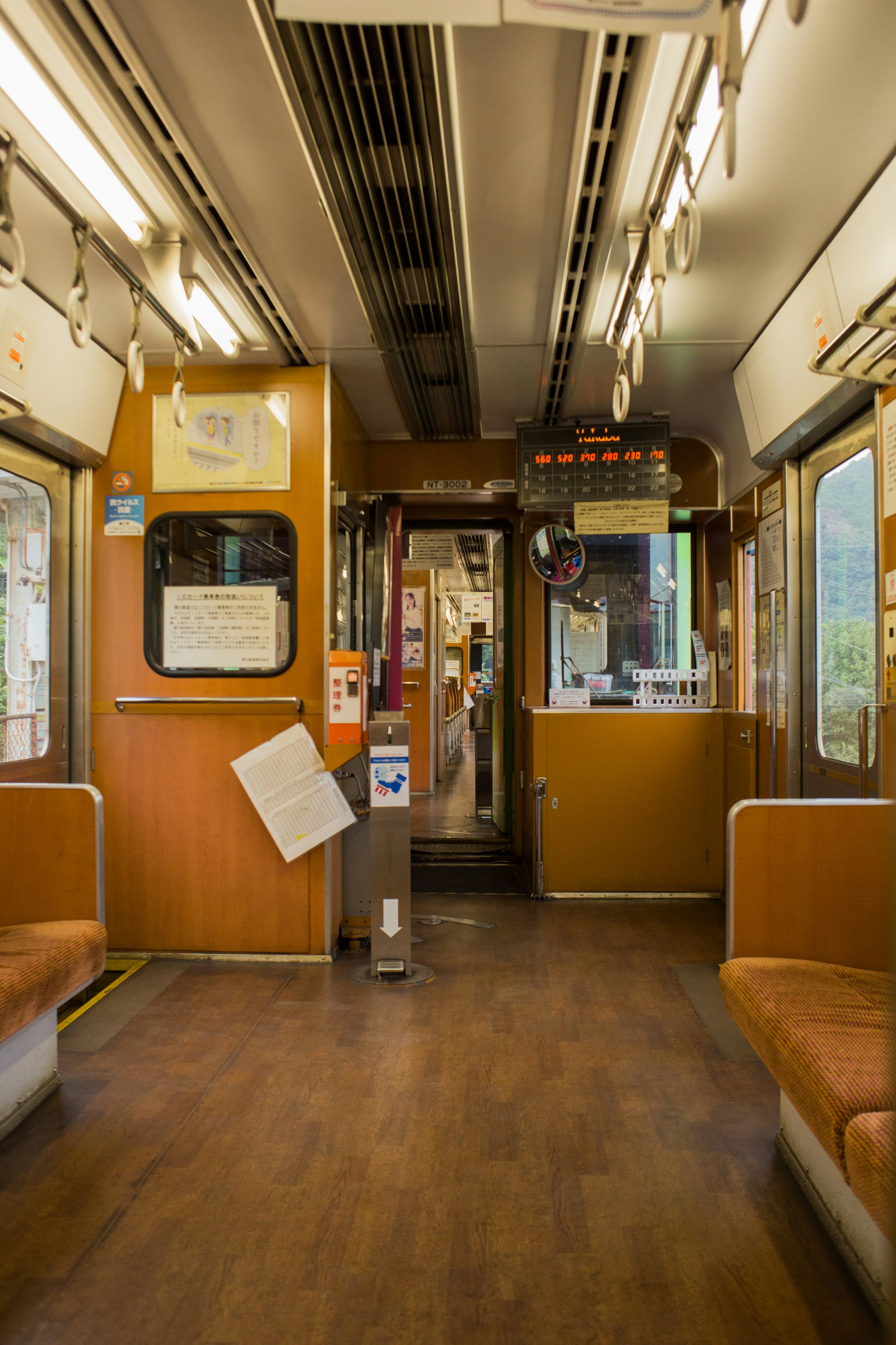 Interior de un vagón de tren con piso de madera y asientos naranjas iluminación brillante y sensación de amplitud