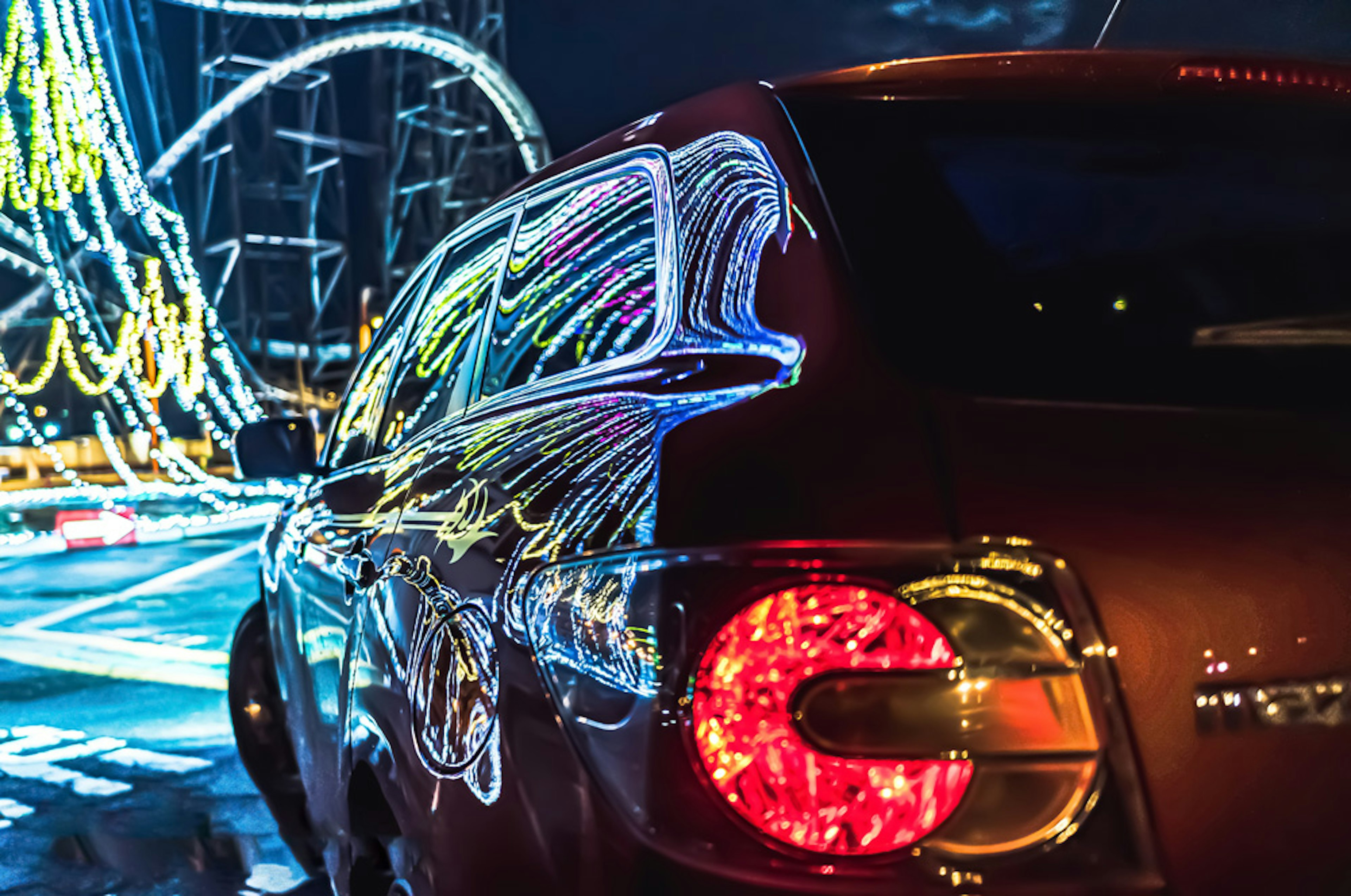 Arrière d'une voiture rouge avec des reflets lumineux colorés sur fond de ville nocturne