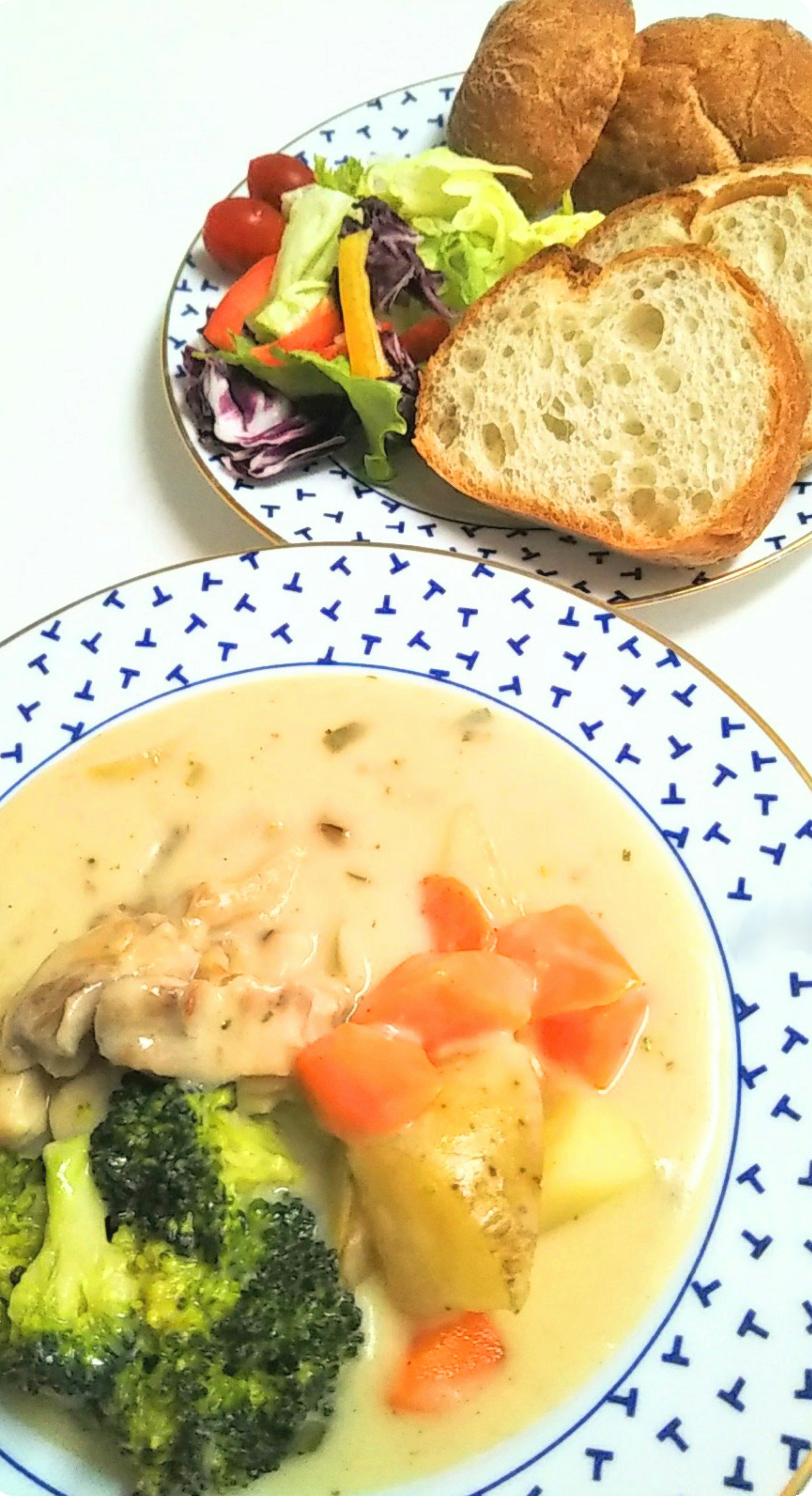 Ein Teller mit cremigem Hühnchen, Brokkoli, Kartoffeln und Karotten serviert mit Salat und Brot