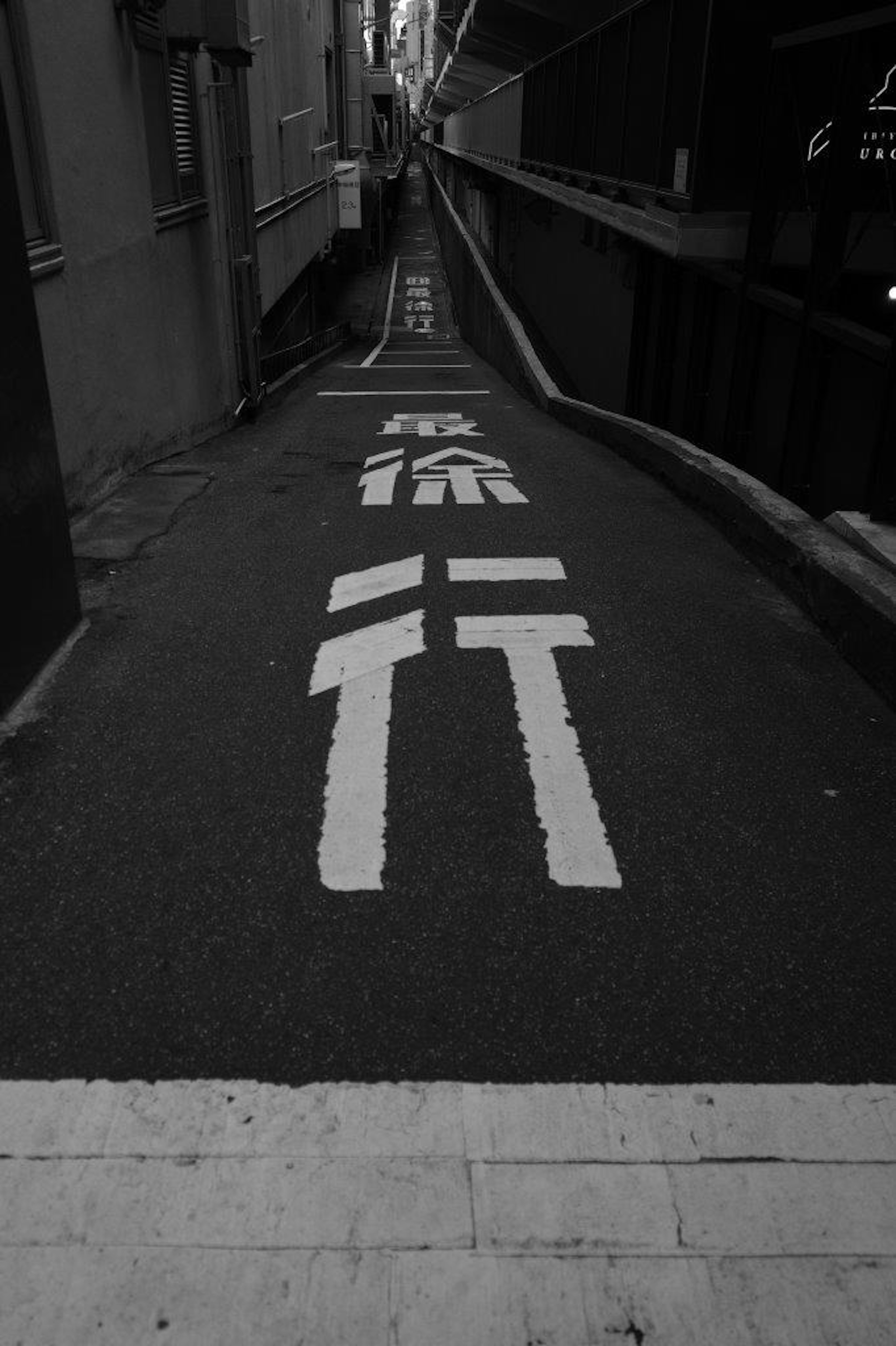 Callejón estrecho con flechas direccionales blancas y texto japonés