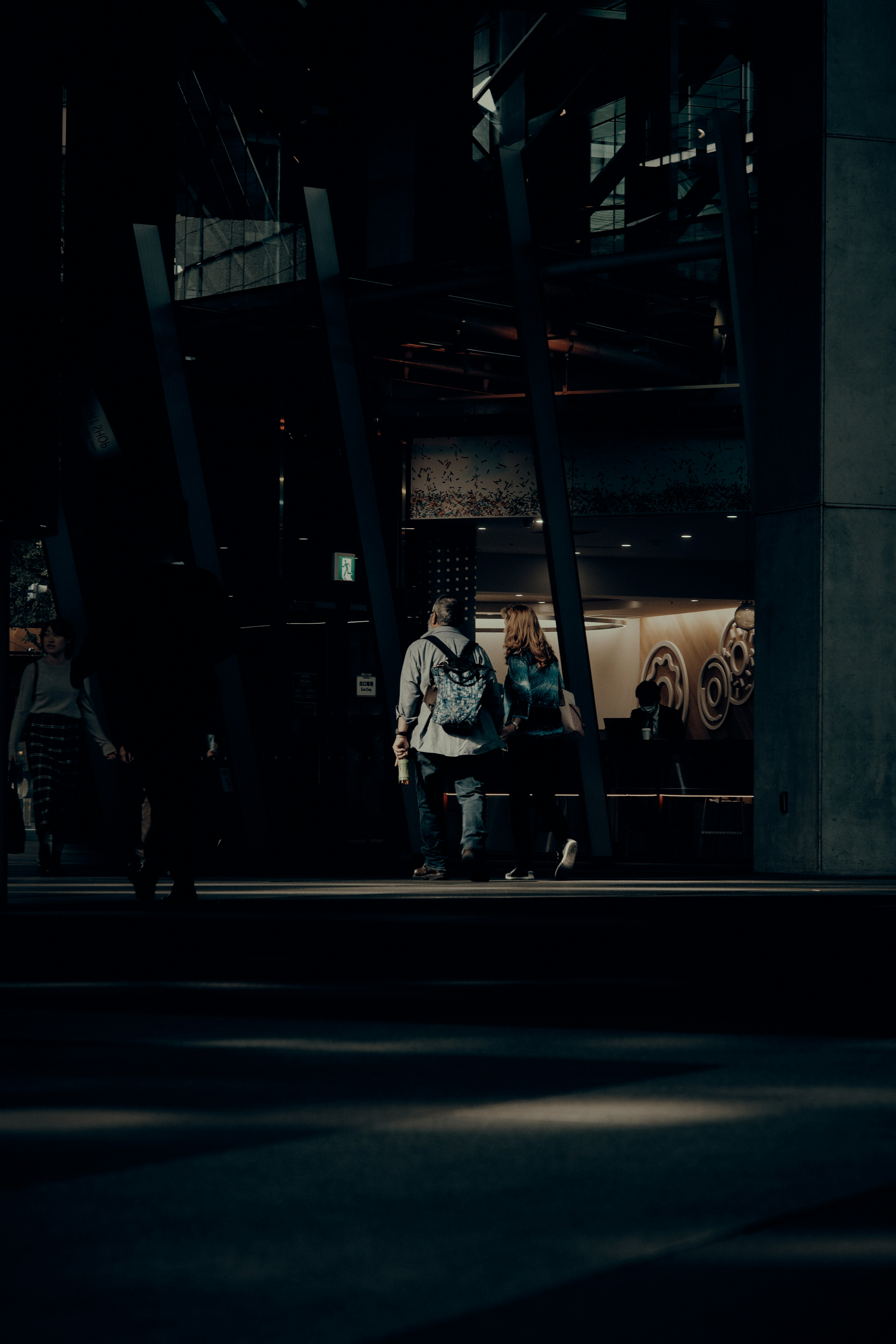 Silhouetten eines Mannes und einer Frau, die auf einer schwach beleuchteten Straße mit einem modernen Gebäude im Hintergrund gehen