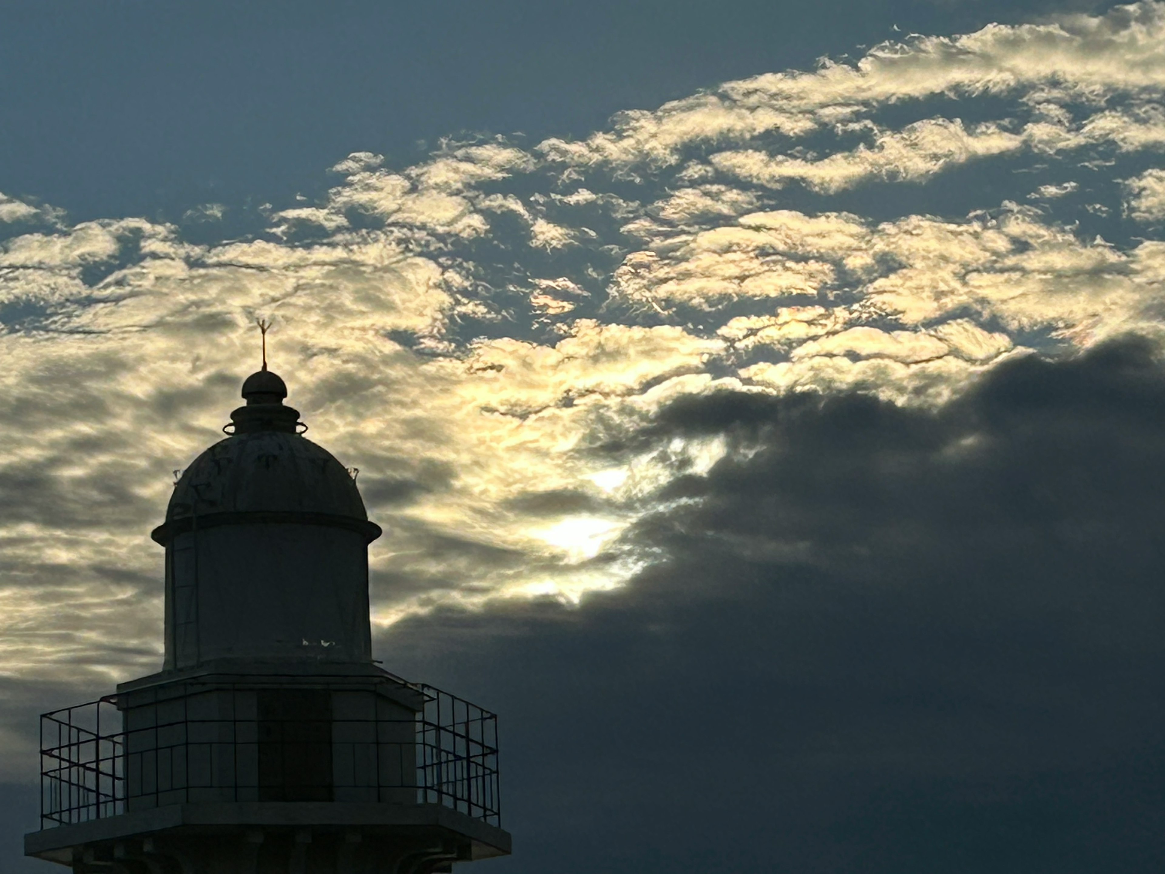 Silueta de un faro contra un fondo de nubes y atardecer