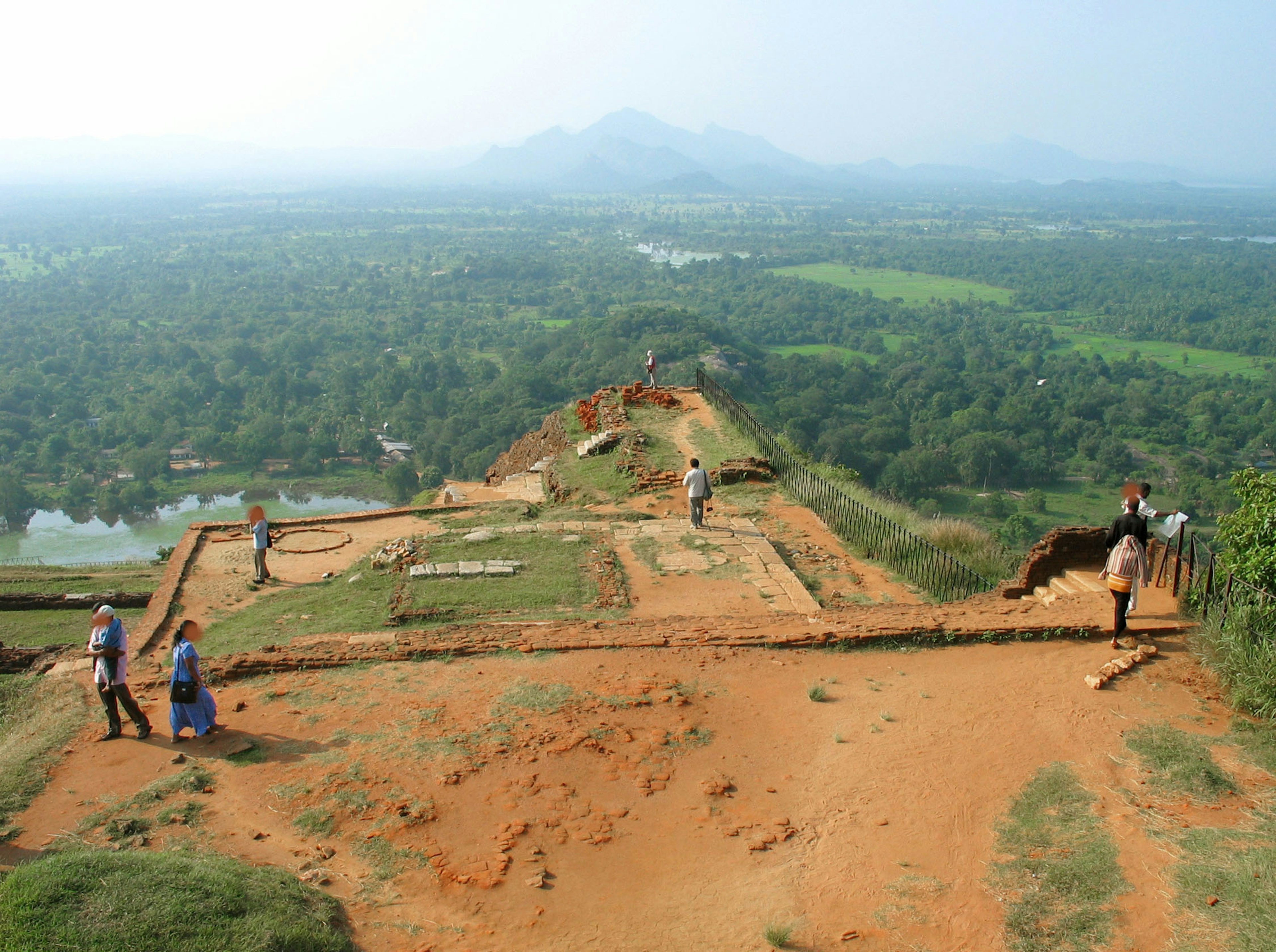 People exploring ancient ruins with lush green landscape in the background