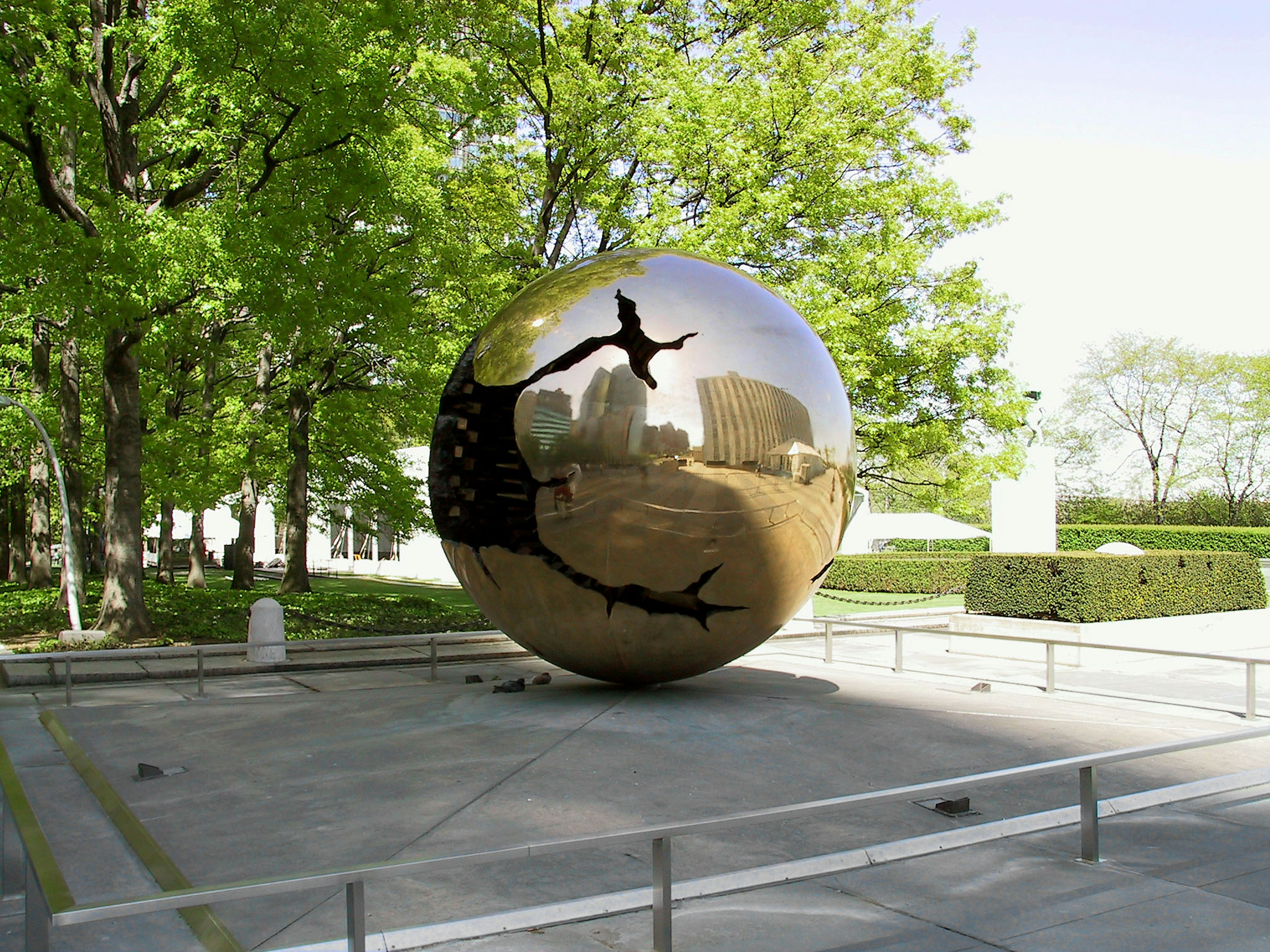 Grande scultura sferica riflettente in un parco circondata da alberi verdi e edifici