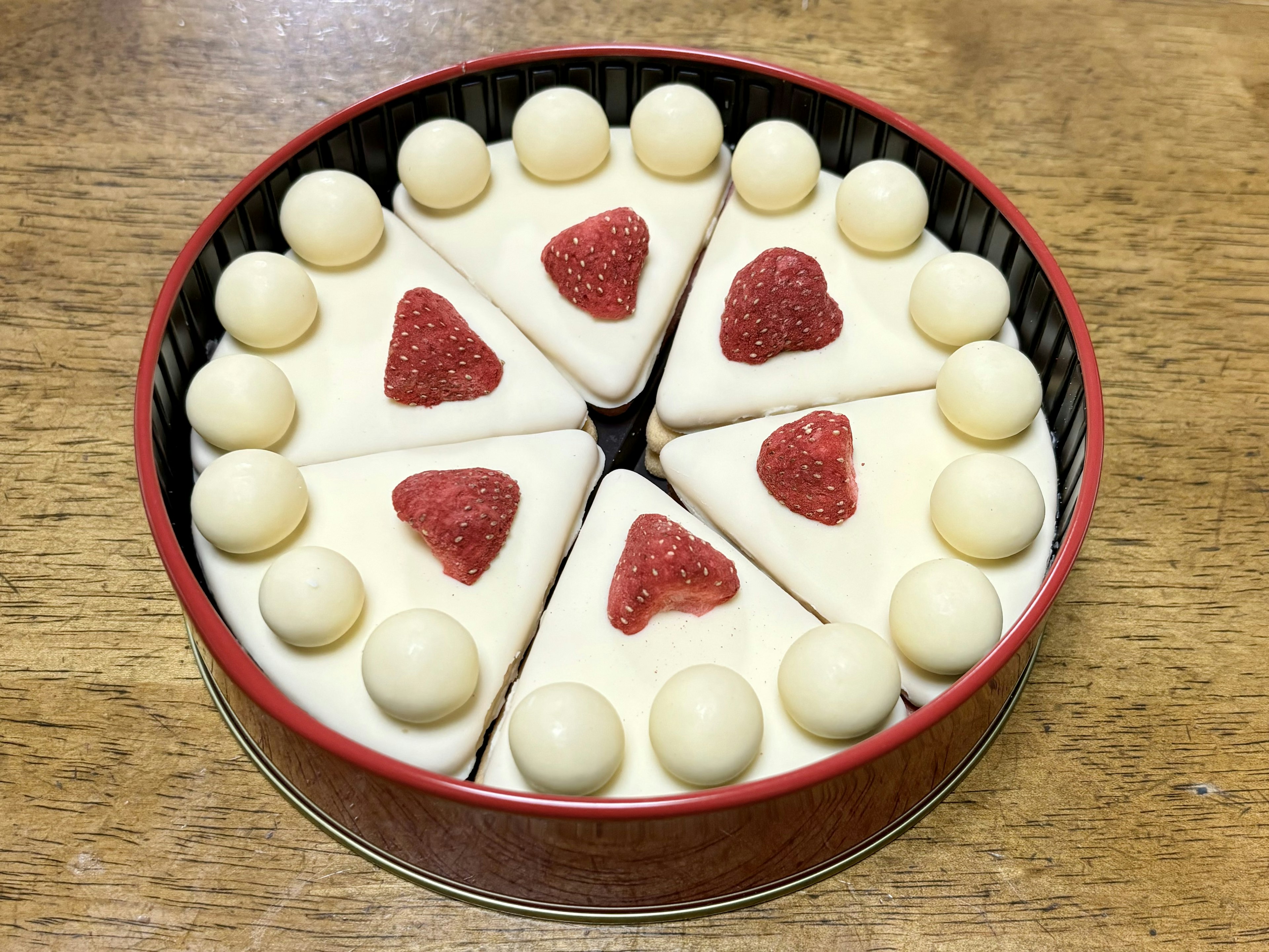 A round tin containing triangular cakes decorated with red hearts and white balls