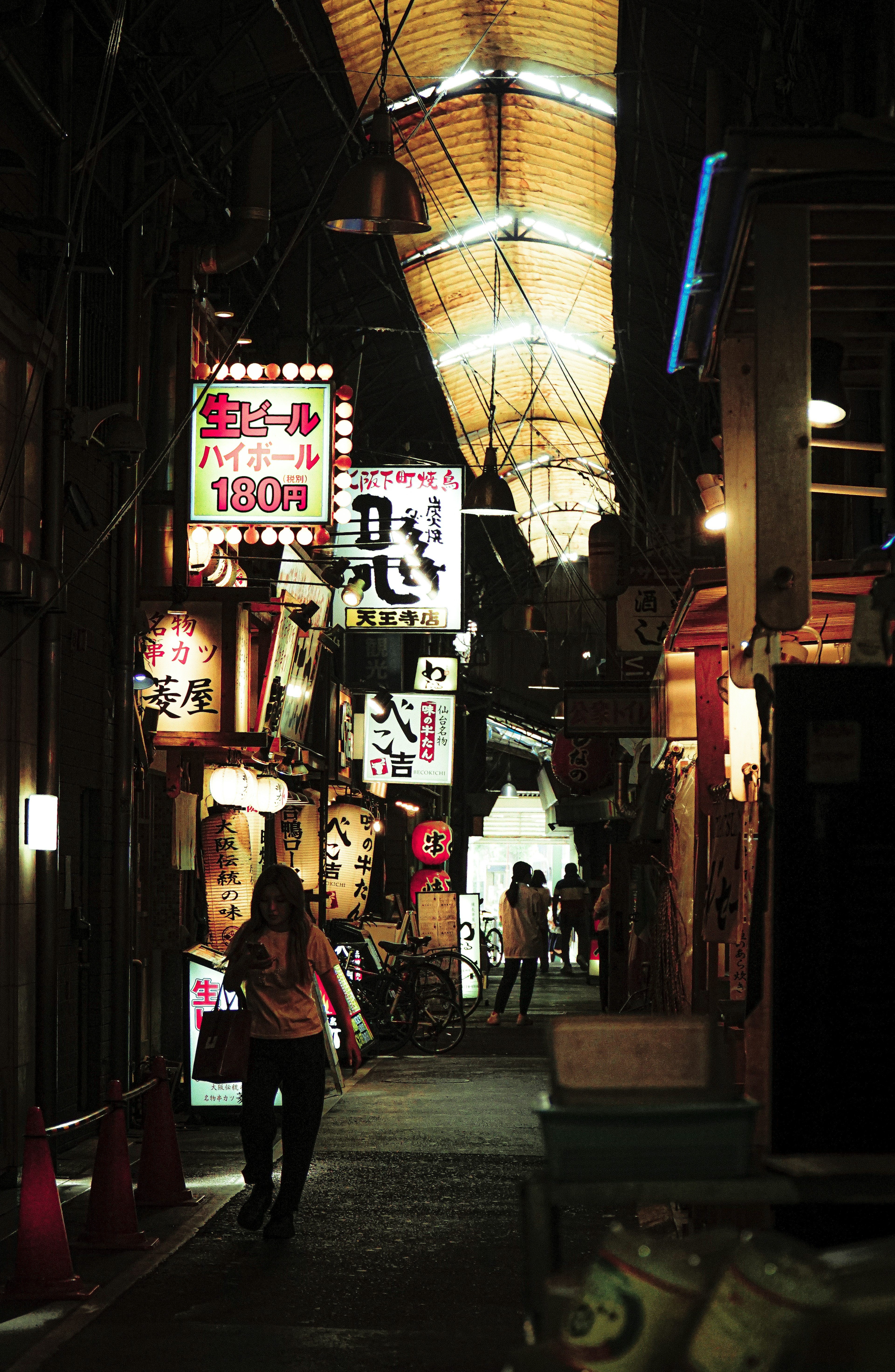 Callejón estrecho bordeado de letreros coloridos y luces que muestran una vibrante escena nocturna