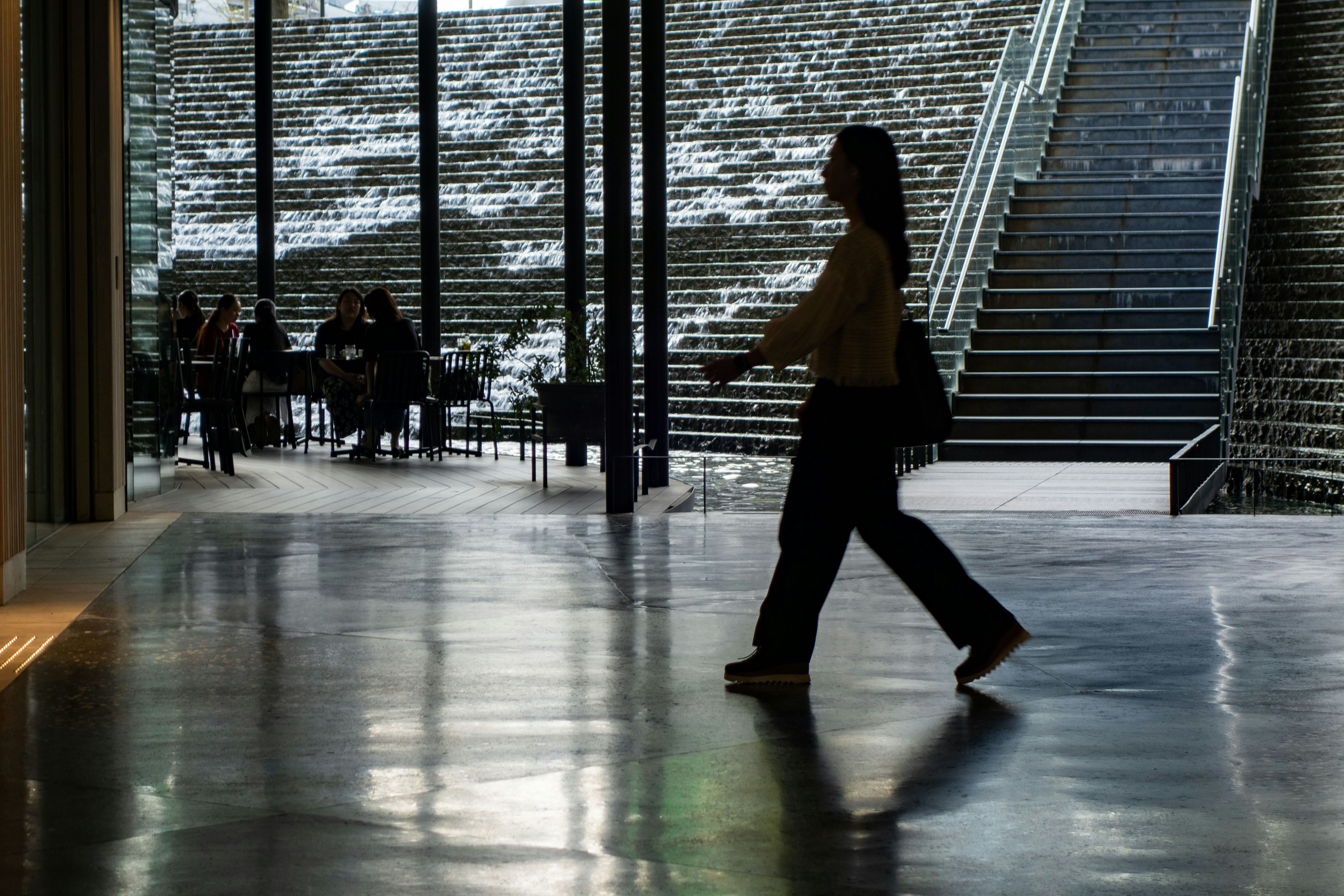 Silhouette di una persona che cammina in un interno di edificio moderno con scale e area salotto sullo sfondo